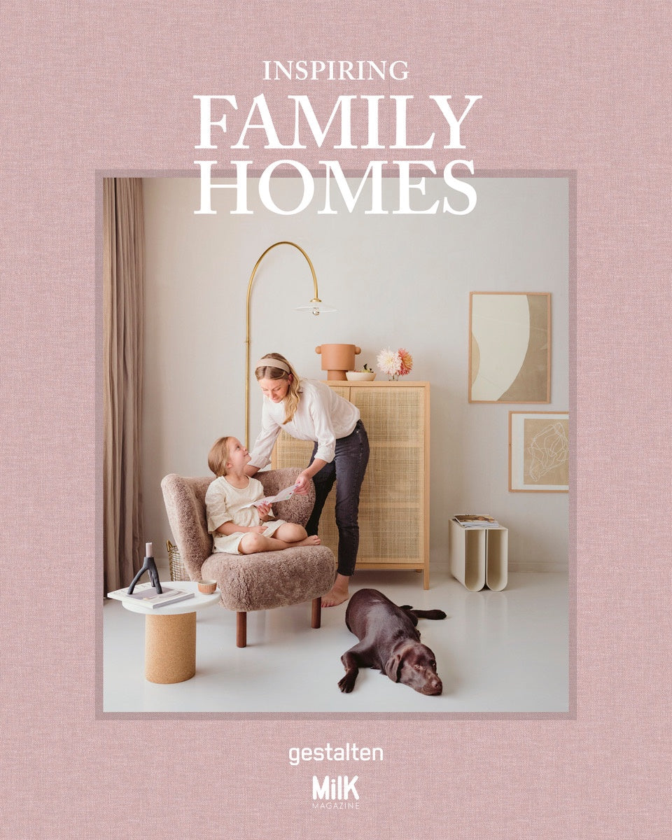 In a cozy living room scene that embodies the essence of INSPIRING FAMILY HOMES - GESTALTEN by Flying Kiwi, a woman and child relax on a plush chair while a brown dog dozes on the floor. The modern interior design features light wood furniture, minimalist art, and soothing neutral tones.
