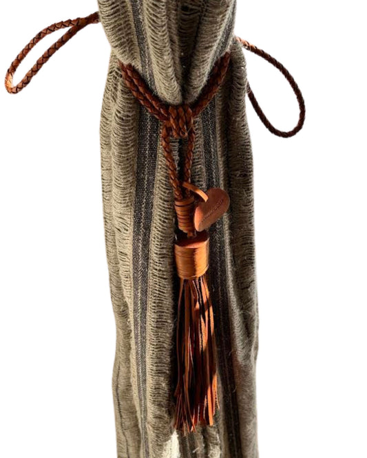 A brown striped curtain is elegantly tied back with The Workroom's Twisted Leather Curtain Tie Backs, featuring a tassel and a heart-shaped charm. This premium accessory complements the bright setting, highlighting the texture of the fabric.