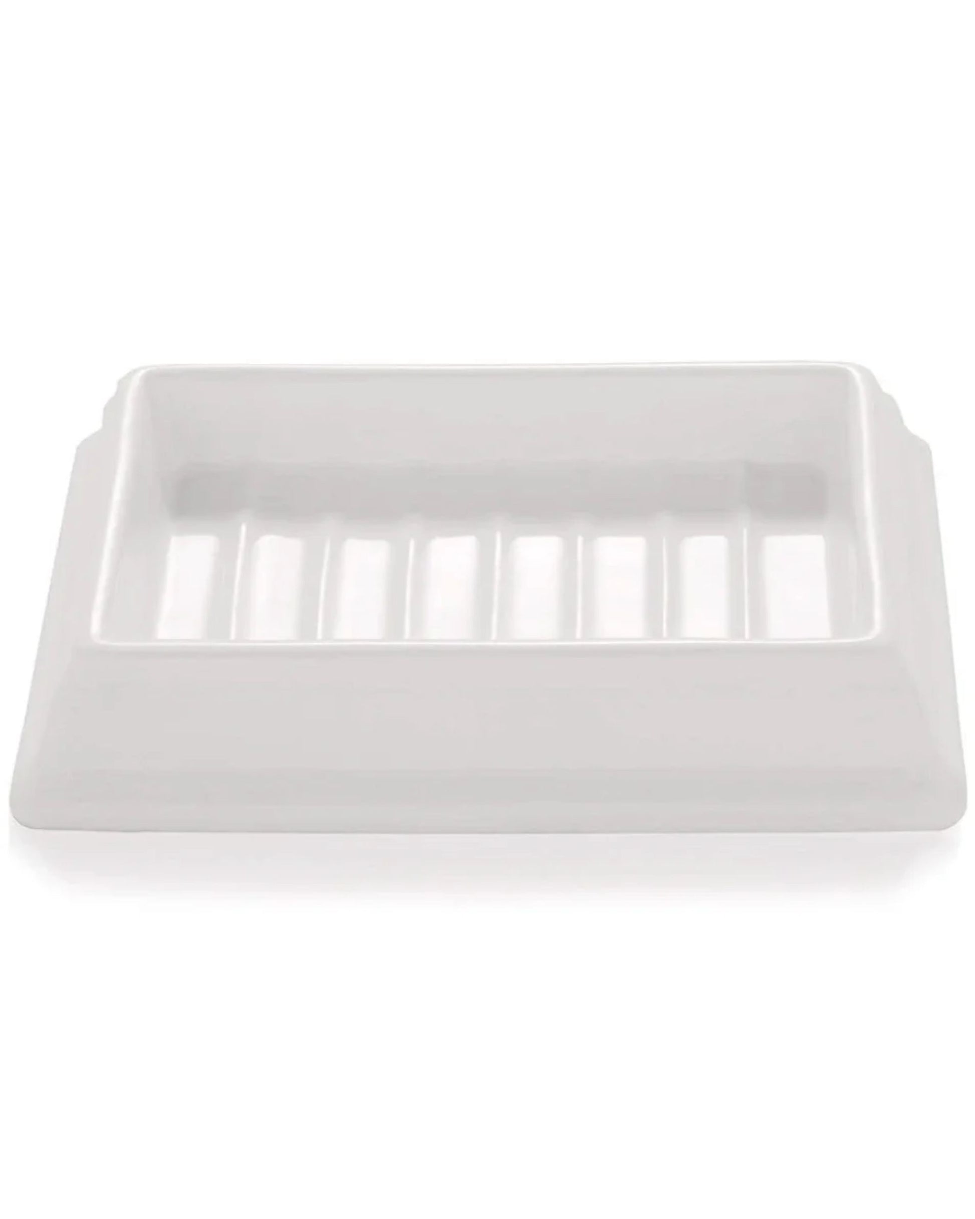 The SORRENTO CERAMIC SOAP DISH by Saison is a rectangular white ceramic dish featuring grooves on the bottom surface, specifically designed to hold a bar of soap. Its simple, minimalist style enhances its organic aesthetic.