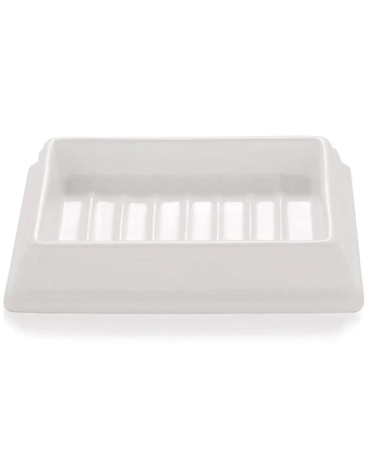 The SORRENTO CERAMIC SOAP DISH by Saison is a rectangular white ceramic dish featuring grooves on the bottom surface, specifically designed to hold a bar of soap. Its simple, minimalist style enhances its organic aesthetic.
