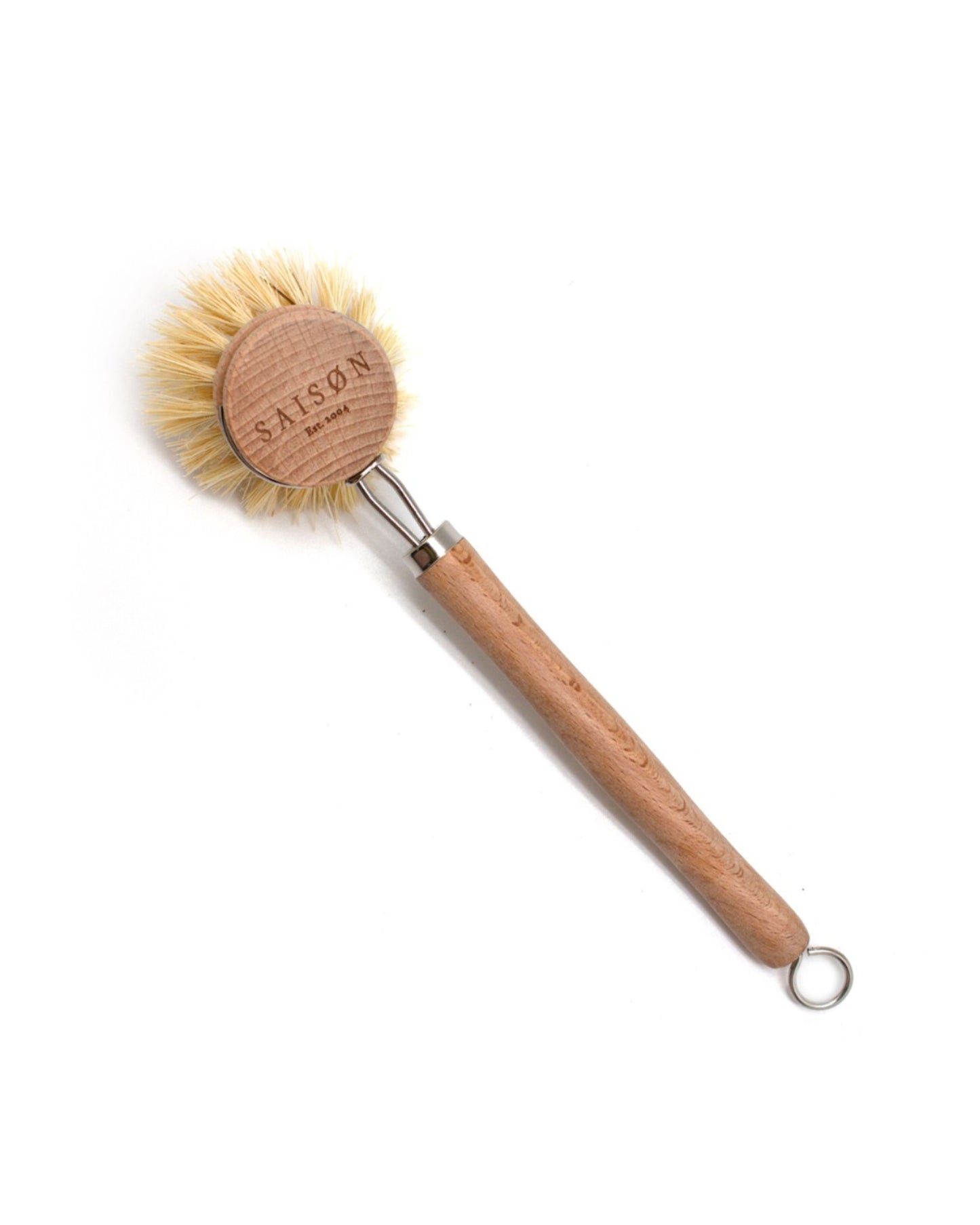 Introducing the Saison ECO BEECH WOOD DISH BRUSH, crafted with a robust beech wood handle and tampico fibre bristles. The brush head is elegantly engraved, and a metal ring at the end of the handle ensures convenient hanging. Ideal for an eco-friendly kitchen, this brush is presented against a white background.