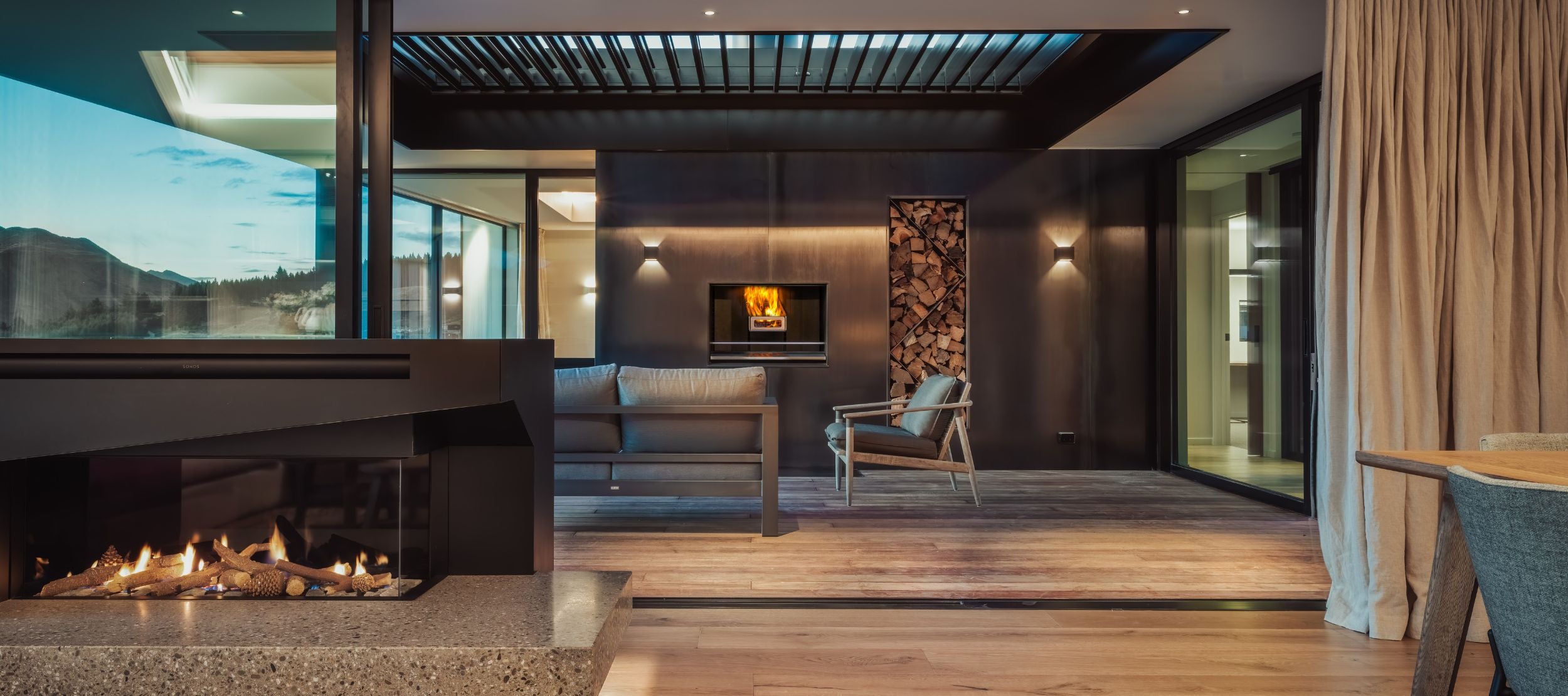 Modern living room with a sleek design, featuring a cozy fireplace, minimalist furniture, and a large sliding glass door offering a view. Warm wood accents complement the neutral color palette, creating a sophisticated and inviting atmosphere.