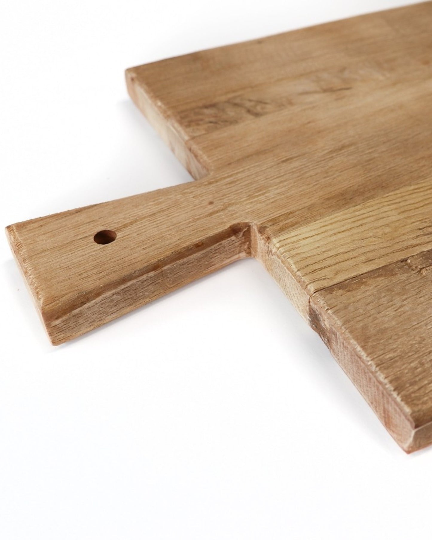 Close-up of the ARTISAN SERVING BOARD - 30cm x 40cm by Hawthorne, featuring a natural wood grain texture and a small hole in its handle for hanging. Part of our Artisan Serving Boards collection, this wooden board is captured at an angle to showcase its thickness, edge details, and the quality craftsmanship characteristic of fine wood products.