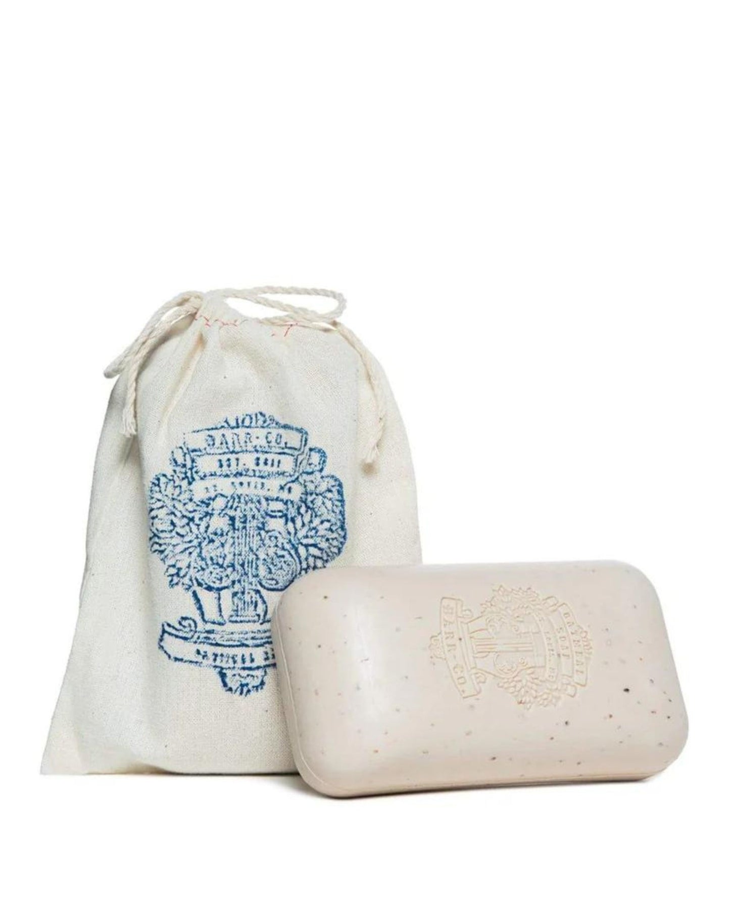 The BARR CO ORIGINAL SADDLE SOAP, a beige bar infused with oatmeal and featuring an embossed Barr Co logo, is placed next to a cream drawstring bag. The bag displays a blue graphic design with intricate details. Both natural items are elegantly set against a plain white background.