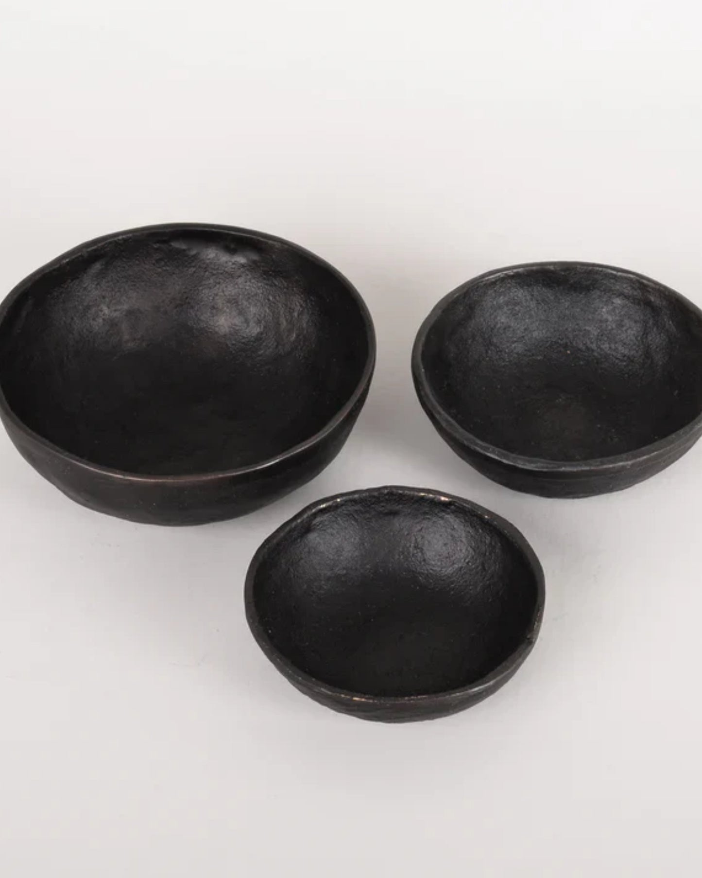 Three BLACK IRON BOWLs from New Direction, each exuding rustic charm, are arranged on a plain white background. The largest bowl is on the left, the medium-sized one on the right, while the smallest sits in front as if they're handmade pieces waiting to tell their unique story.