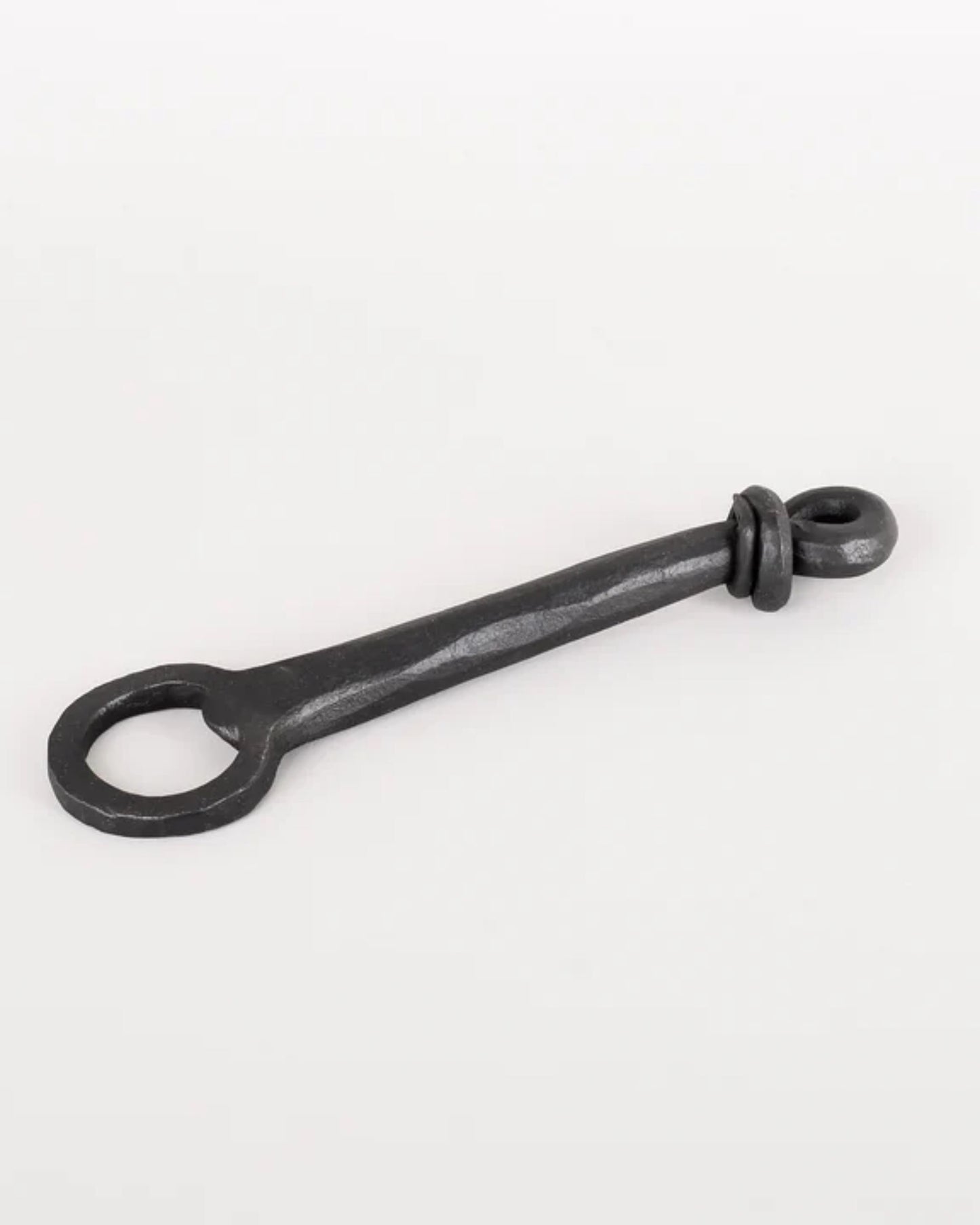 The BLACK IRON BOTTLE OPENER W/ KNOT END by New Direction exudes rustic charm with its long handle. It features a distinctive loop at one end and a smaller rounded hook at the other, all set against a plain white background to highlight its handmade elegance.