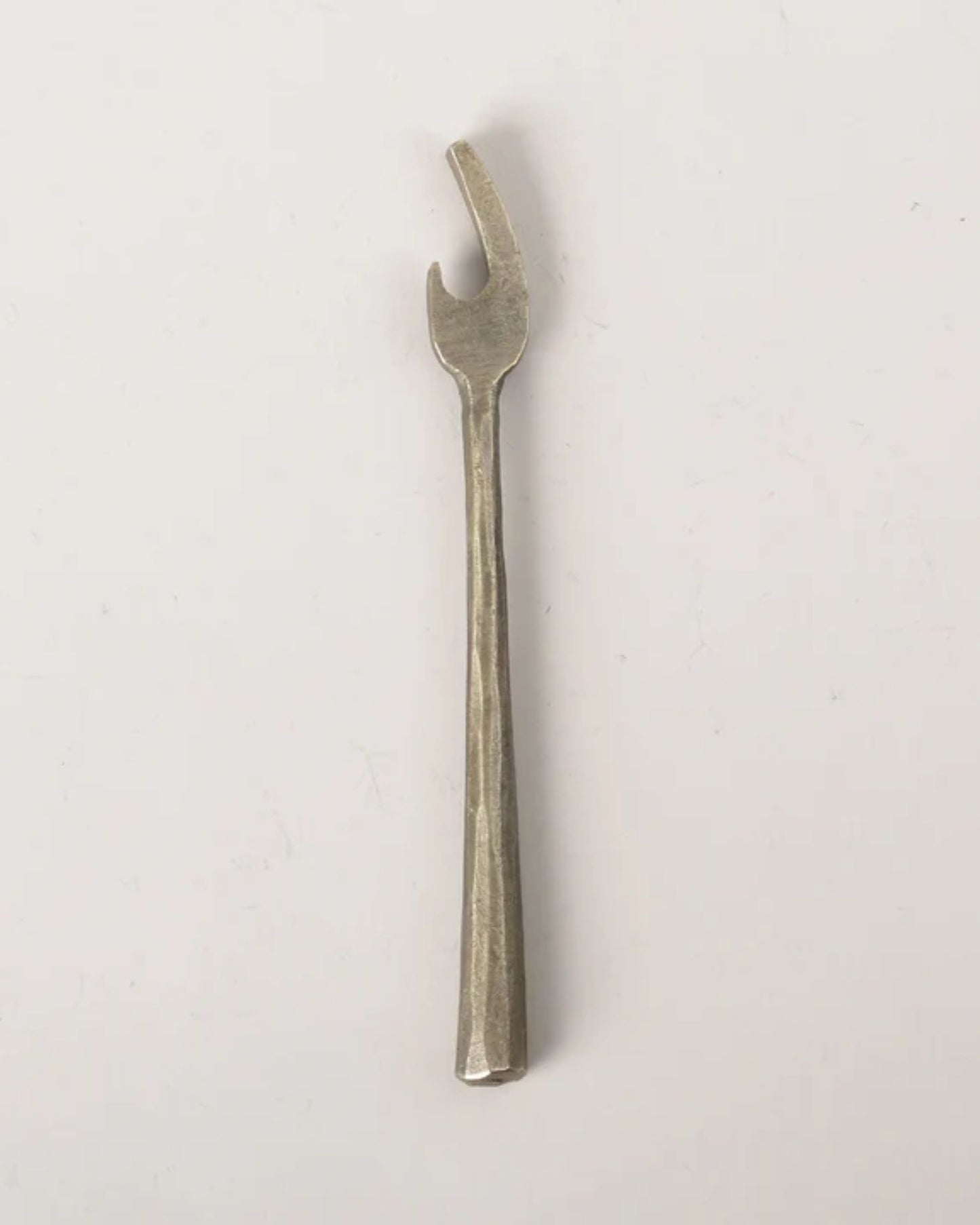 The BRASS WRENCH BOTTLE OPENER by New Direction, featuring a long handle and hooked end, exudes industrial charm. Its vintage-inspired design makes it a standout piece against a plain white background.