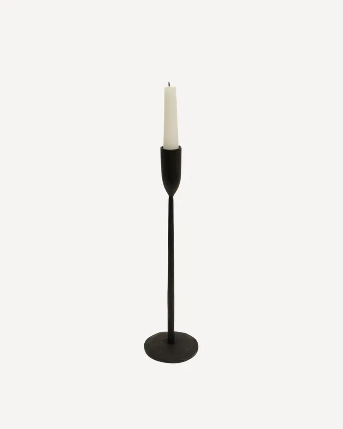 The DAX Candleholder by French Country is a minimalist, hand-forged black piece featuring a slim, tall stand and a circular base. Crafted from matte black cast iron, it elegantly showcases a white taper candle against a plain light background.