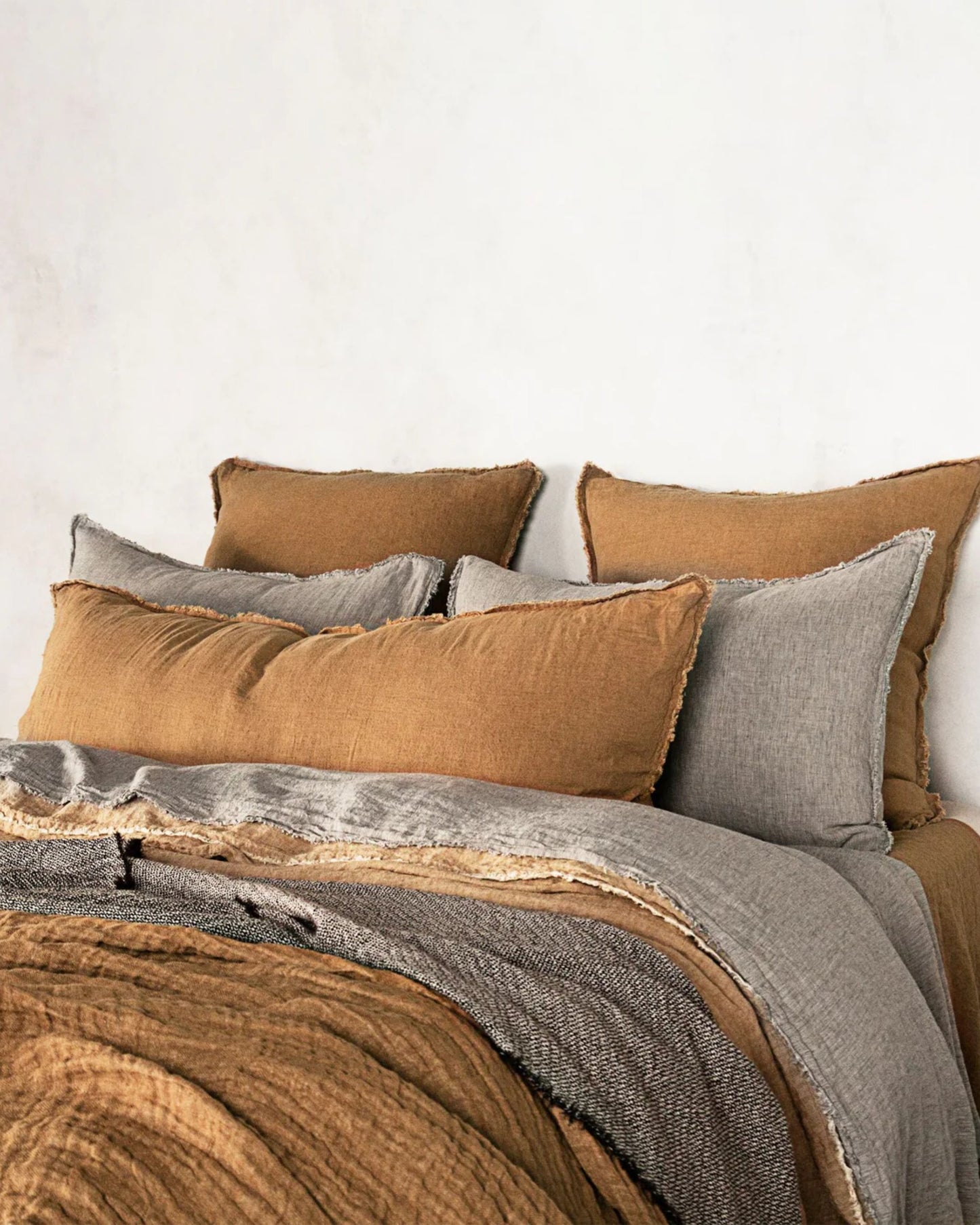 A neatly made bed features plush pillows adorned with the Hale Flocca Body Pillow Case by Hale Mercantile Co, along with blankets in shades of brown and gray. The cozy, textured bedding stands out against a plain white wall, creating a warm and inviting atmosphere.