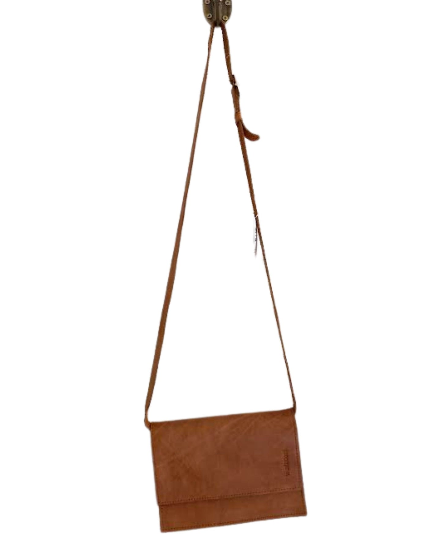 The LEATHER FLAT STRAP PURSE by The Workroom, crafted from brown full-grain leather, hangs on a hook, proudly showcasing its place in the accessory collection. Featuring a simple flap design with a long, flat strap and minimalist stitching, it is perfect for those who appreciate understated elegance.