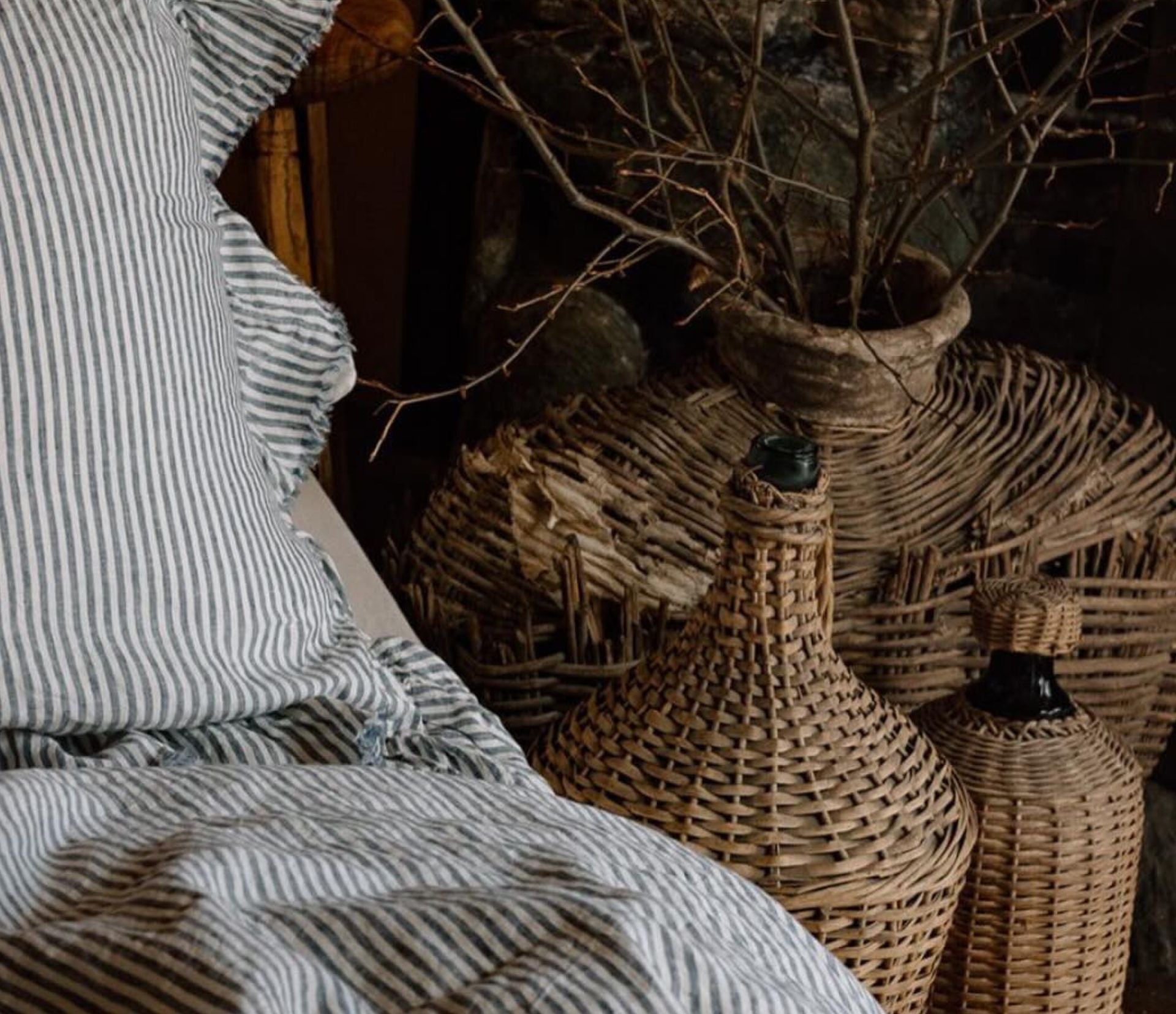 A cozy scene featuring striped bedding and large woven baskets in various shapes and sizes. The baskets are adorned with dried branches, adding a rustic touch to the setting.
