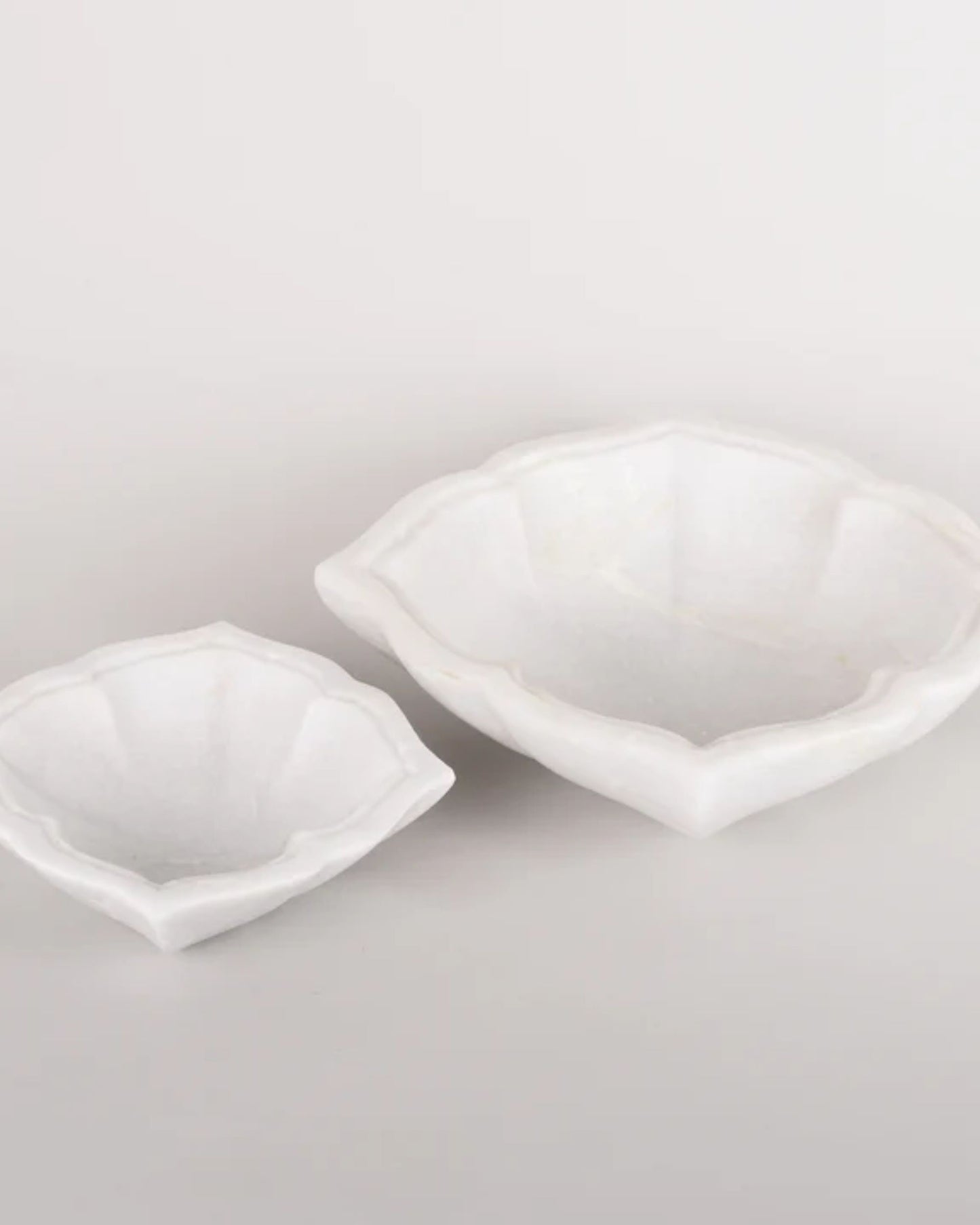 A set of Flower Marble Bowls from New Direction, each featuring a floral-inspired shape with scalloped edges, is crafted from authentic marble. Their smooth and glossy finish enhances any plain background with an elegant decorative touch.