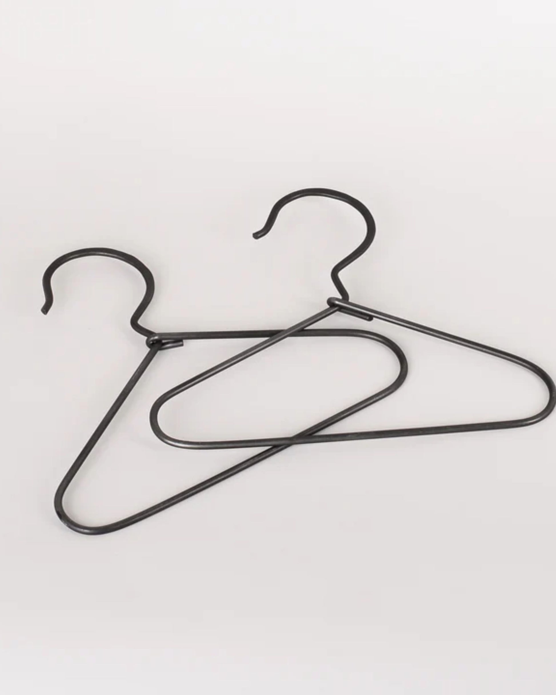 Two MINI BURNISHED COAT HANGERS from New Direction overlap against a plain white background. Their minimalist design features hooks at the top, and they are positioned at different angles, creating an aesthetic that exudes both elegance and simplicity.