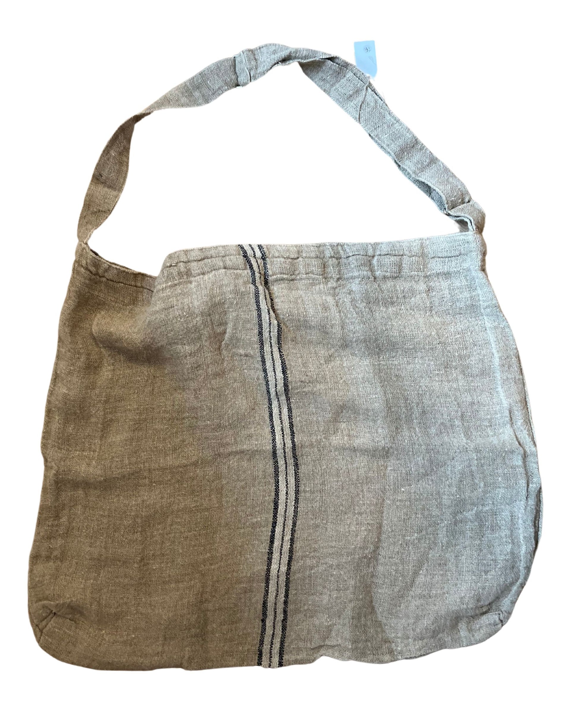 The OVERSIZED BAG NAVY MIDDLE STRIPE HANDLOOMED from Rustic Linen is a beige linen shoulder bag with a straightforward design, featuring a single broad strap. Its rustic charm is enhanced by a vertical navy stripe along the middle, and it is crafted from lightweight, textured material that is also anti-allergenic.