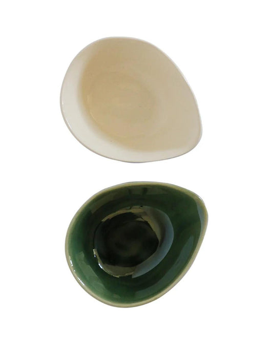 Two PETITE BOWLs from CC interiors, each with a small and irregular shape, rest on a white background. The top bowl features a cream color, while the bottom one is dark green. Both bowls boast an organic design and smooth surface, adding a slightly asymmetrical charm to enhance your dining experience.