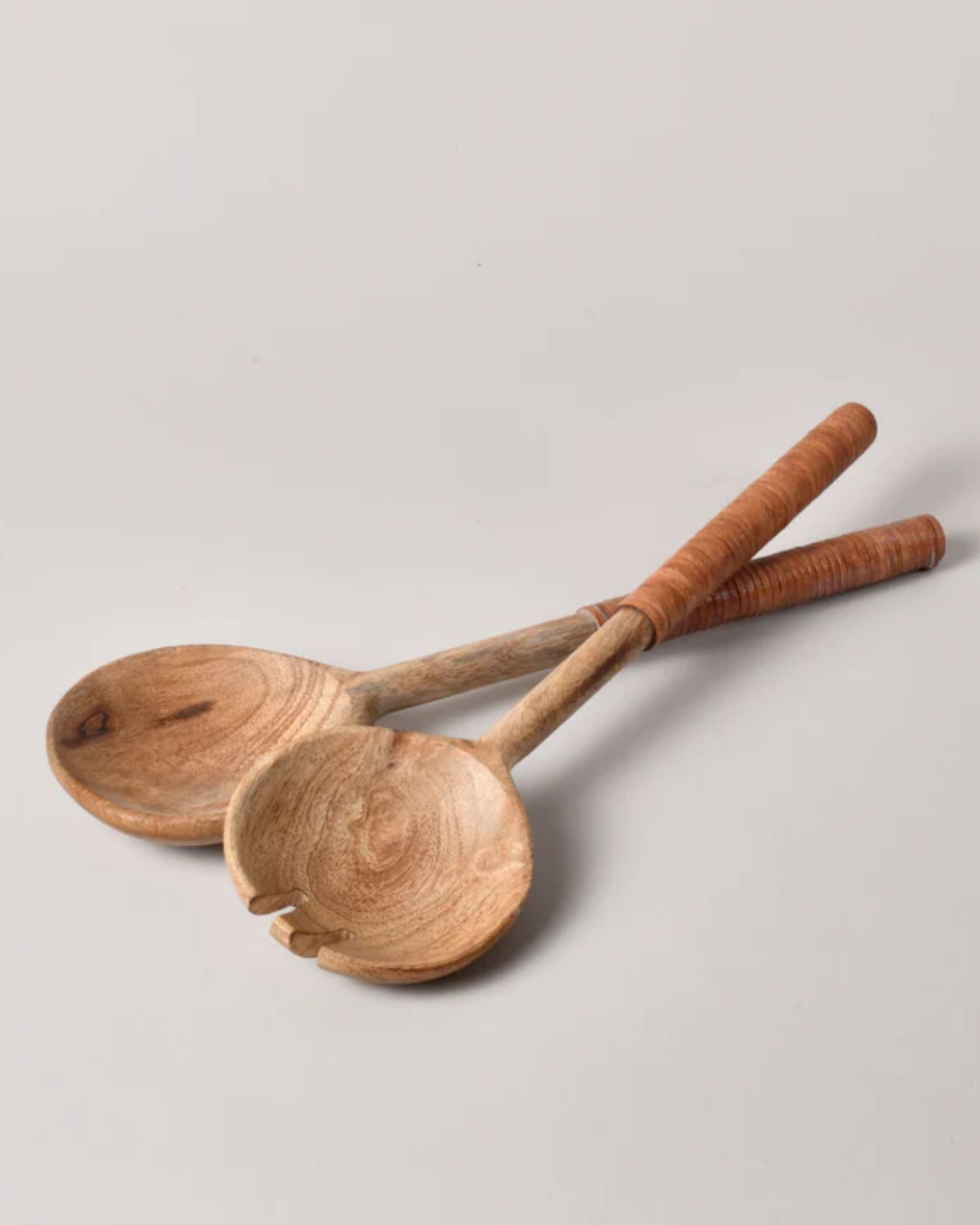 Two SALAD SERVER W/LEATHER HANDLE from New Direction are crafted from mango wood, featuring wide, rounded ends and long handles elegantly wrapped in light brown material, resting gracefully on a plain surface.