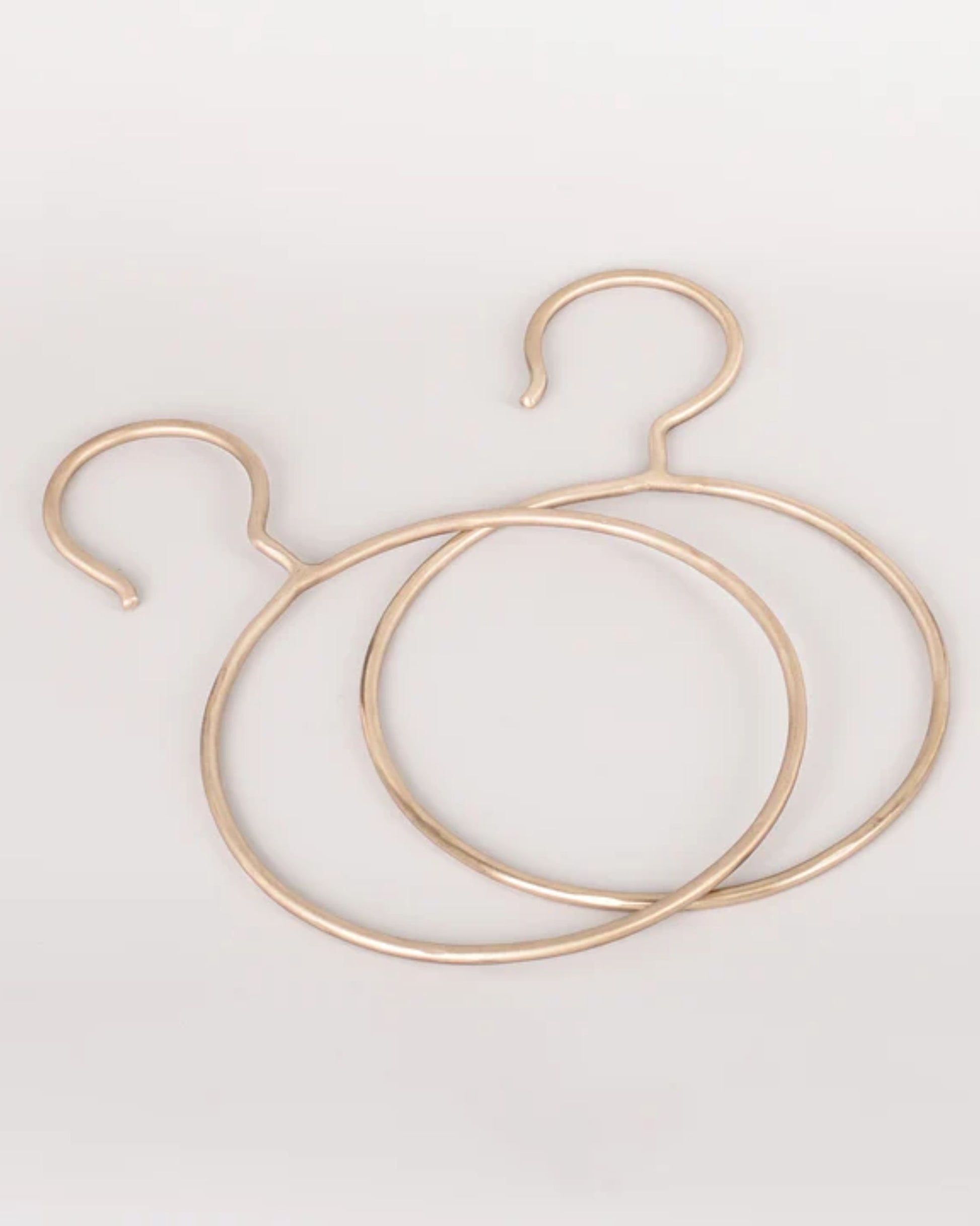 Product: Two gold-colored, circular metal items from New Direction's SOLID BRASS SCARF DISPLAY collection are positioned on a plain white background. These handmade pieces showcase a closed circle with one end curving outward like a hook, making them both stylish and functional accessories.