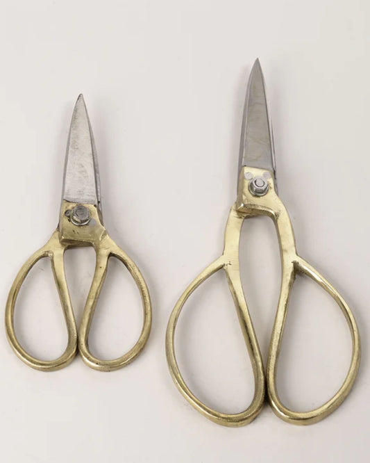 Positioned against a light gray background, this set of cutting tools shines with elegance and durability. The ergonomic design of New Direction's THICK BONZA SCISSORS ensures comfort and style, featuring one smaller pair on the left alongside a larger pair on the right. Both pairs are adorned with gleaming blades and elaborate gold handles.