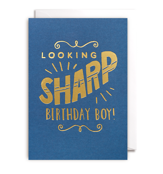 A blue greeting card named "LOOKING SHARP BIRTHDAY BOY" by Oxted features the text "Looking Sharp Birthday Boy!" in bold gold letters. The word "Sharp" is embellished with stylized lines for a dynamic effect, and the card is displayed slightly open.