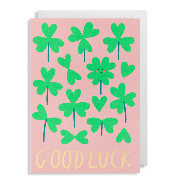 The Oxted GOOD LUCK - GREETING CARD features a pink background adorned with green shamrocks and hearts, with the words GOOD LUCK written in yellow at the bottom.