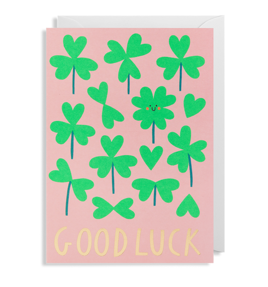 The Oxted GOOD LUCK - GREETING CARD features a pink background adorned with green shamrocks and hearts, with the words GOOD LUCK written in yellow at the bottom.