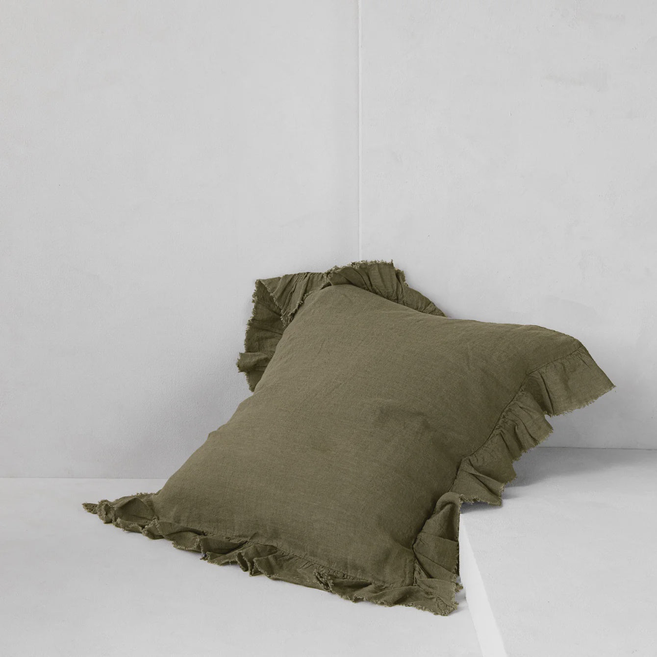 The HALE KRISTINE EURO PILLOWCASE by Hale Mercantile Co, with its ruffled edges and vintage-inspired design, rests against a light grey wall. It is slightly slanted on a minimalistic and clean surface, adding a touch of charm to the bedroom decor.