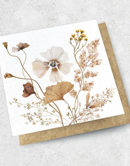 The DRIED ARRANGEMENT - GREETING CARD by The Workroom showcases a premium textured design with watercolor depictions of delicate, dried flowers and leaves in earthy tones. It is elegantly presented on a kraft envelope against a light, textured background.