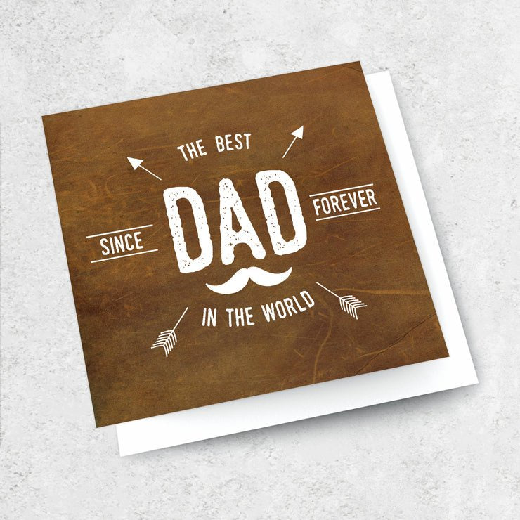 The "THE BEST DAD IN THE WORLD - GIFT CARD" by Ink Bomb features a brown background with white text reading "The Best Dad Since Forever In The World," accented with arrows and a mustache graphic. The card is displayed on a white envelope set against a light backdrop.