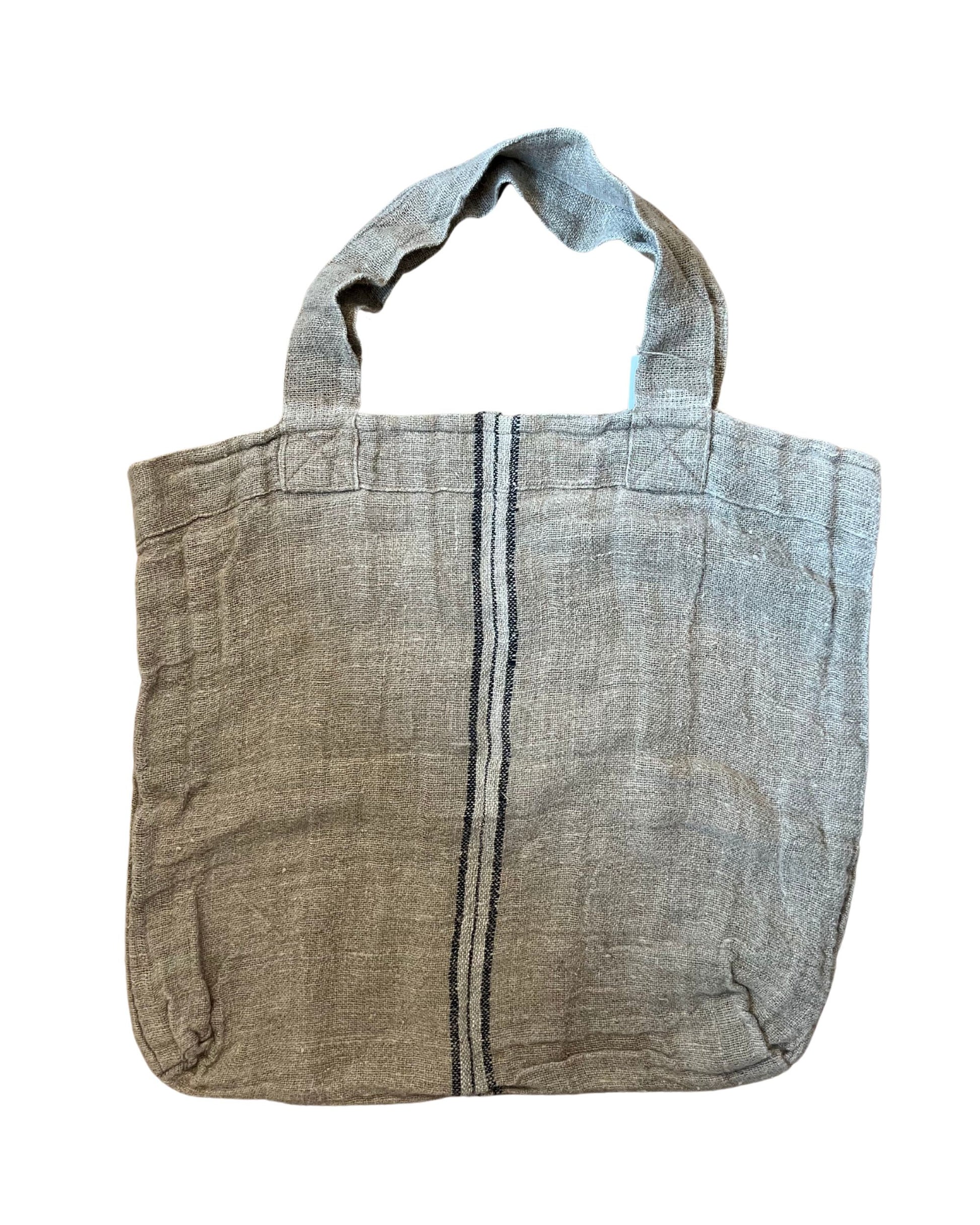 Introducing the Rustic Linen Angaston Hand-Loomed Tote Bag: a charming rustic beige tote featuring two short handles and a single vertical navy stripe near the center. It showcases a textured, slightly worn appearance, highlighting the beauty of 100% pure linen.