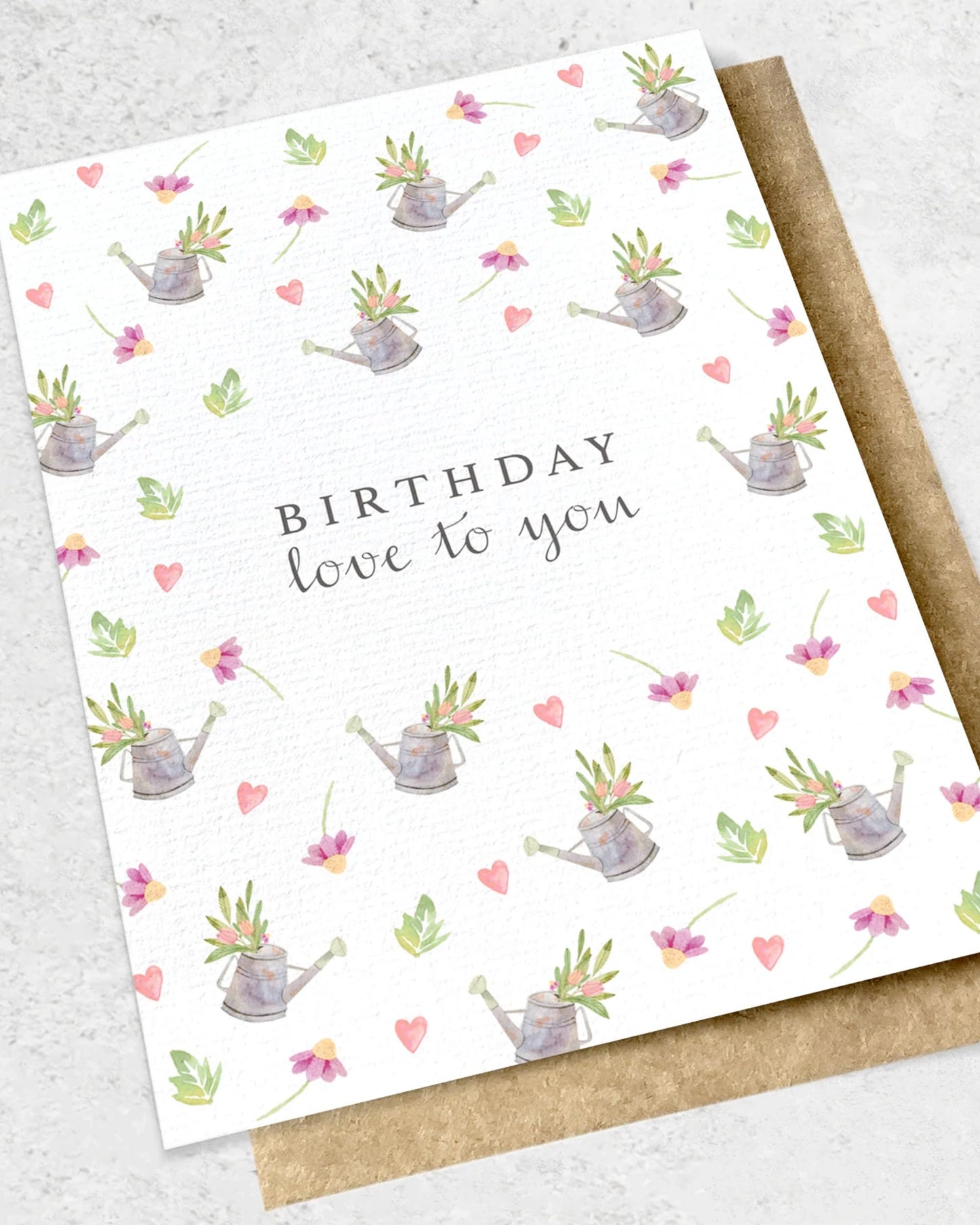 The Ink Bomb BIRTHDAY LOVE TO YOU - WATERING CANS GREETING CARD features a premium textured design with the message "Birthday love to you," beautifully accented by illustrations of watering cans, flowers, leaves, and hearts on a white background. It comes elegantly paired with a classic kraft envelope.