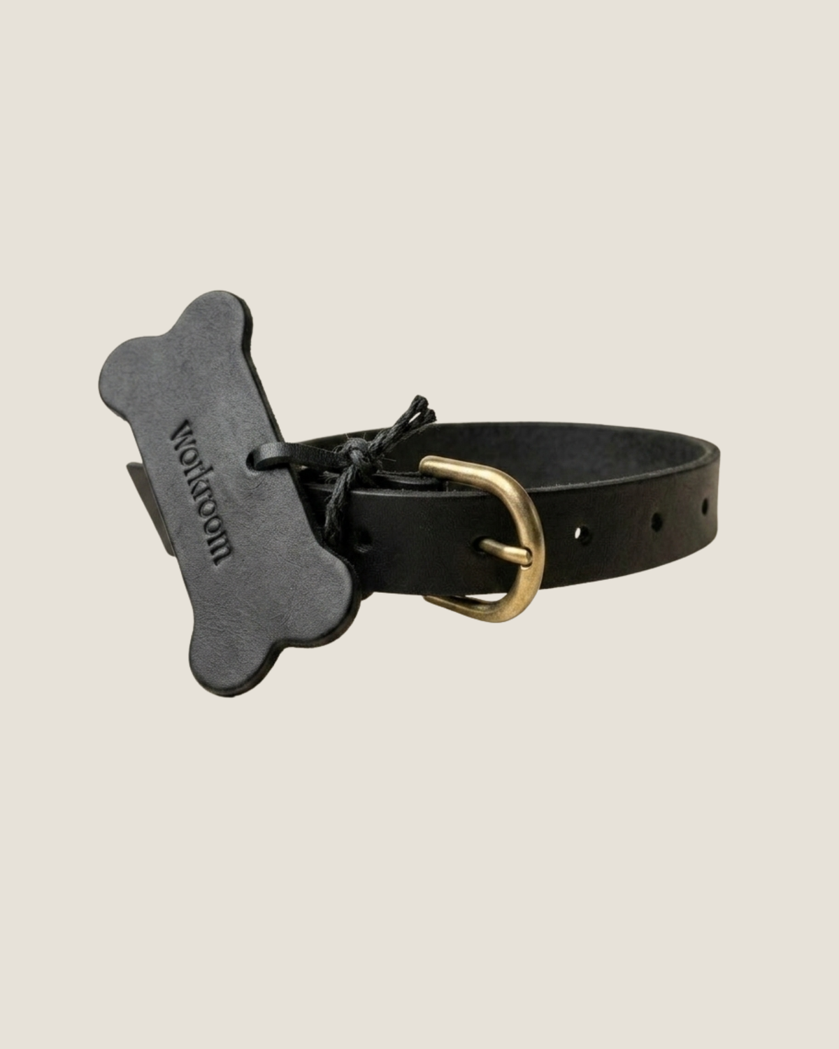 The Workroom's FLAT DOG COLLARS are crafted from premium leather and come adorned with a bone-shaped tag that reads  designed to resemble a dog biscuit. These collars feature a gold buckle, multiple adjustment holes, and robust hardware for lasting durability.