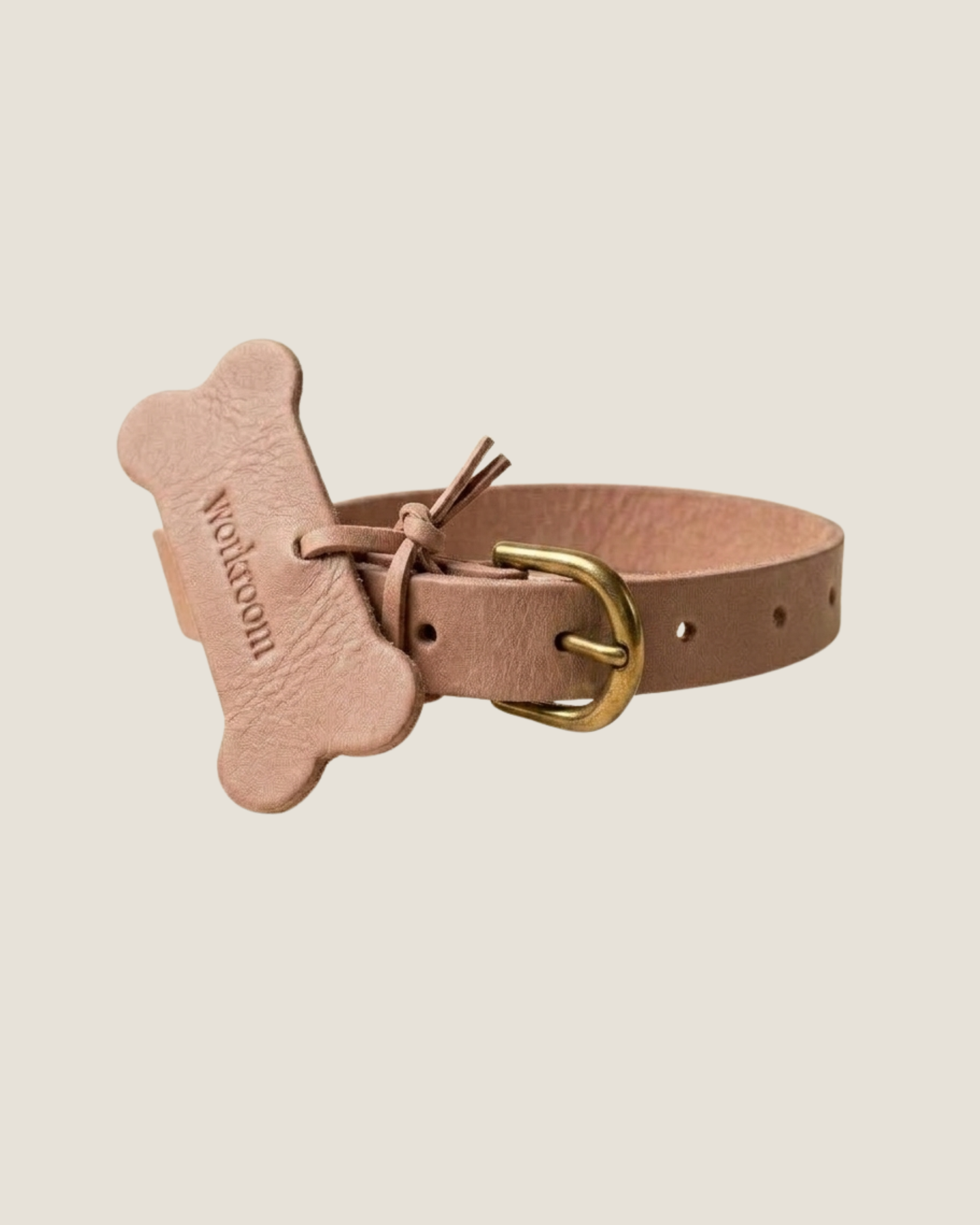 The Workroom's FLAT DOG COLLARS are crafted from premium leather and come adorned with a bone-shaped tag that reads  designed to resemble a dog biscuit. These collars feature a gold buckle, multiple adjustment holes, and robust hardware for lasting durability.