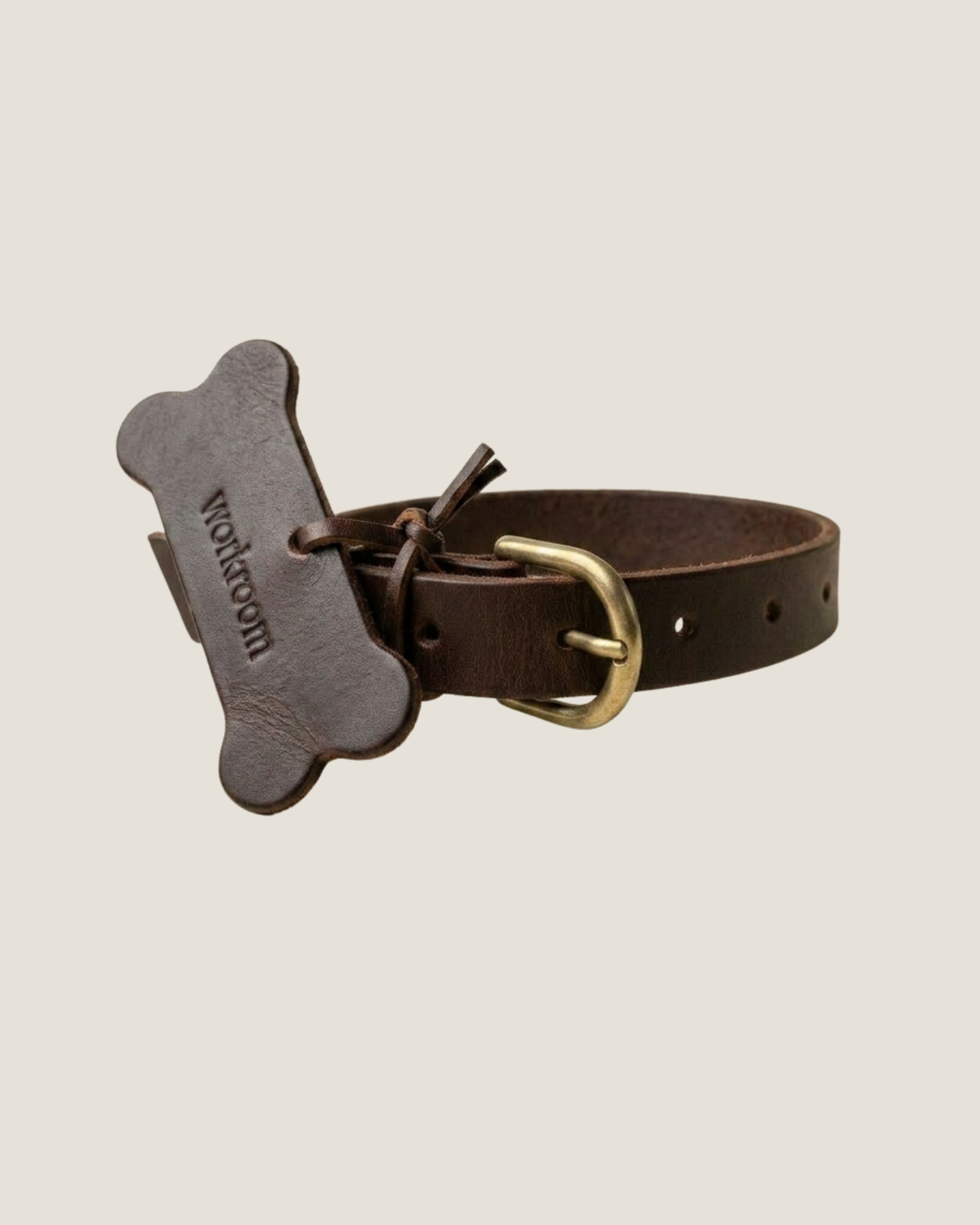 The Workroom's FLAT DOG COLLARS are crafted from premium leather and come adorned with a bone-shaped tag that reads  designed to resemble a dog biscuit. These collars feature a gold buckle, multiple adjustment holes, and robust hardware for lasting durability.
