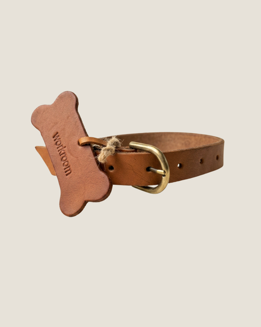 The Workroom's FLAT DOG COLLARS are crafted from premium leather and come adorned with a bone-shaped tag designed to resemble a dog biscuit. These collars feature a gold buckle, multiple adjustment holes, and robust hardware for lasting durability.