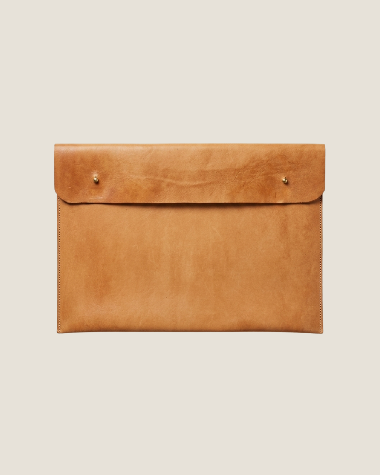 The elegant LEATHER LAPTOP COVER by The Workroom is a large brown envelope-style clutch crafted from 100% leather, featuring a smooth texture and two small metal studs on the front. Its visible stitching along the edges makes it perfect for use as a chic leather laptop case.