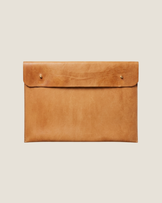The elegant LEATHER LAPTOP COVER by The Workroom is a large brown envelope-style clutch crafted from 100% leather, featuring a smooth texture and two small metal studs on the front. Its visible stitching along the edges makes it perfect for use as a chic leather laptop case.