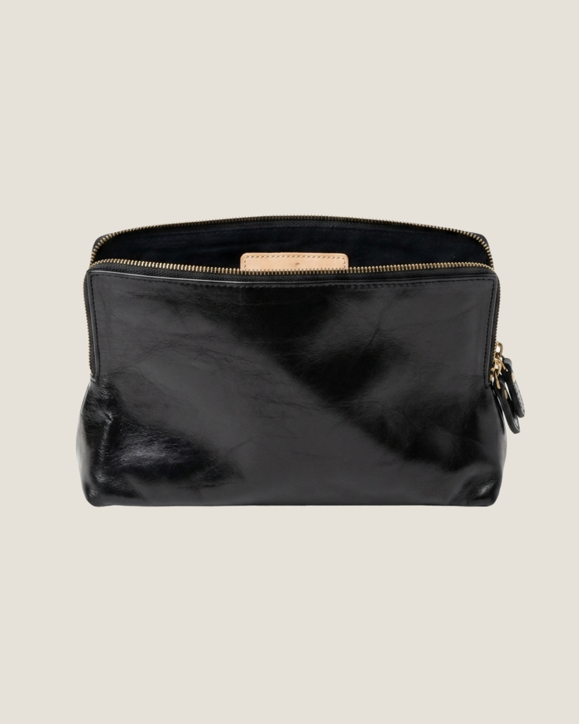 The LEATHER ZIP COSMETIC BAG by The Workroom features a black full-grain leather exterior  open to reveal its soft and smooth texture. This pouch is ideal for organizing your beauty routine and exudes elegance