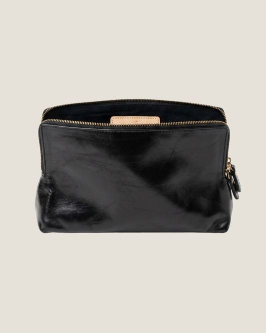 The LEATHER ZIP COSMETIC BAG by The Workroom features a black full-grain leather exterior  open to reveal its soft and smooth texture. This pouch is ideal for organizing your beauty routine and exudes elegance
