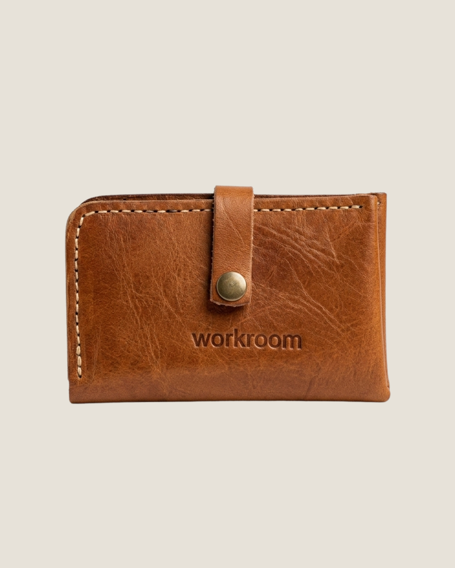 The LEATHER COIN/CARD WALLET by The Workroom is a classic brown leather accessory featuring a button closure and the brand's name expertly embossed on the front. Crafted from full-grain leather, it showcases visible stitching along the edges, combining elegance with durability.