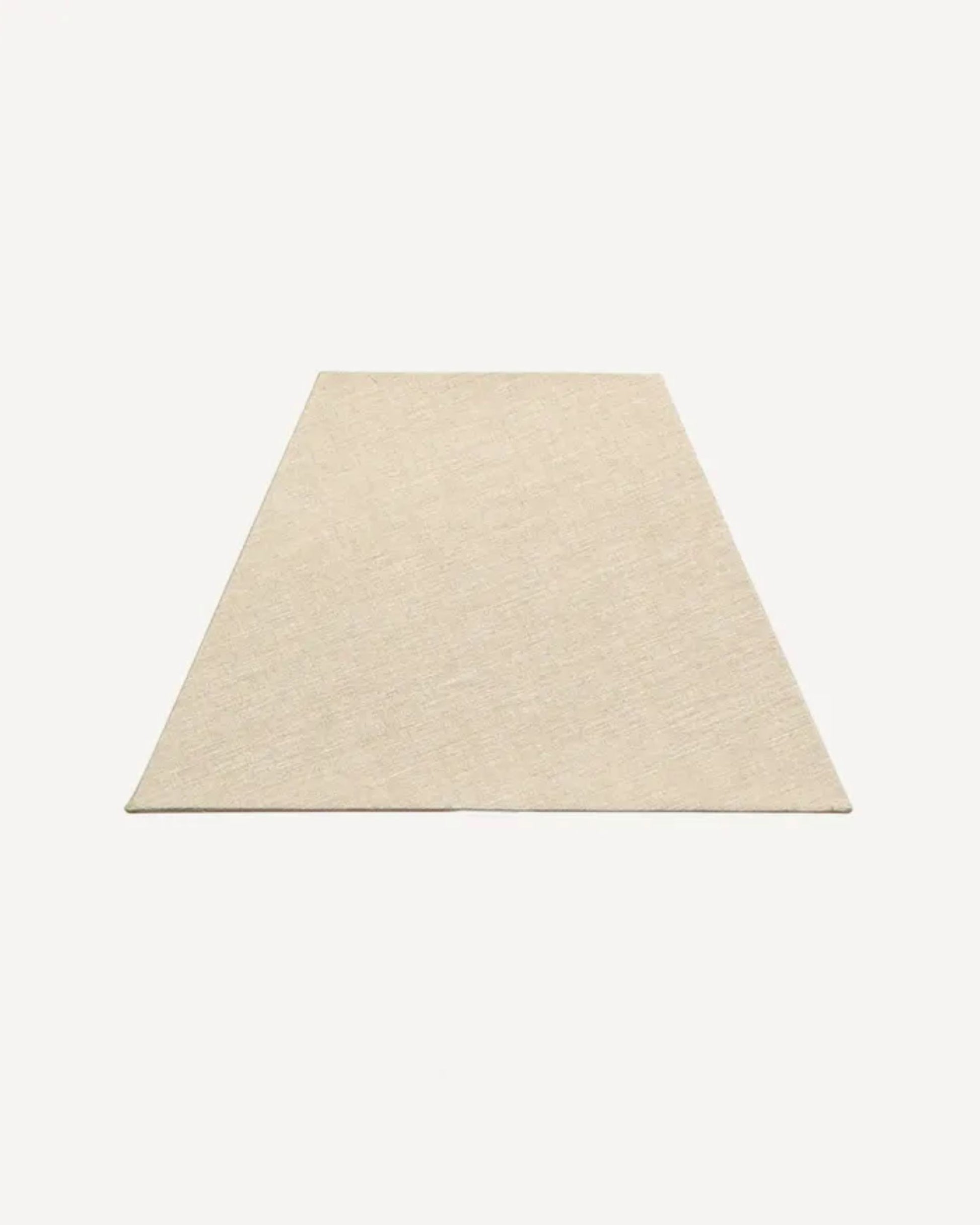 A beige, trapezoidal rug is laid flat against a neutral background, its shorter edge closer to the viewer, exuding minimalist charm. Nearby, a French Country RECTANGLE SHADE LINEN NATURAL 41X28CM adds a touch of nostalgia with its European fittings.