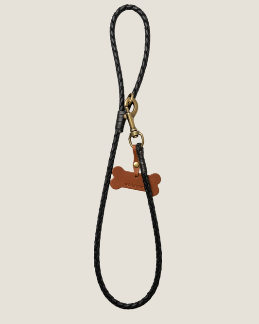 Introducing *The Workroom Roped Leather Dog Lead*: a stylish black braided accessory with a durable metal clip and an elegant bone-shaped tag crafted from premium brown leather.