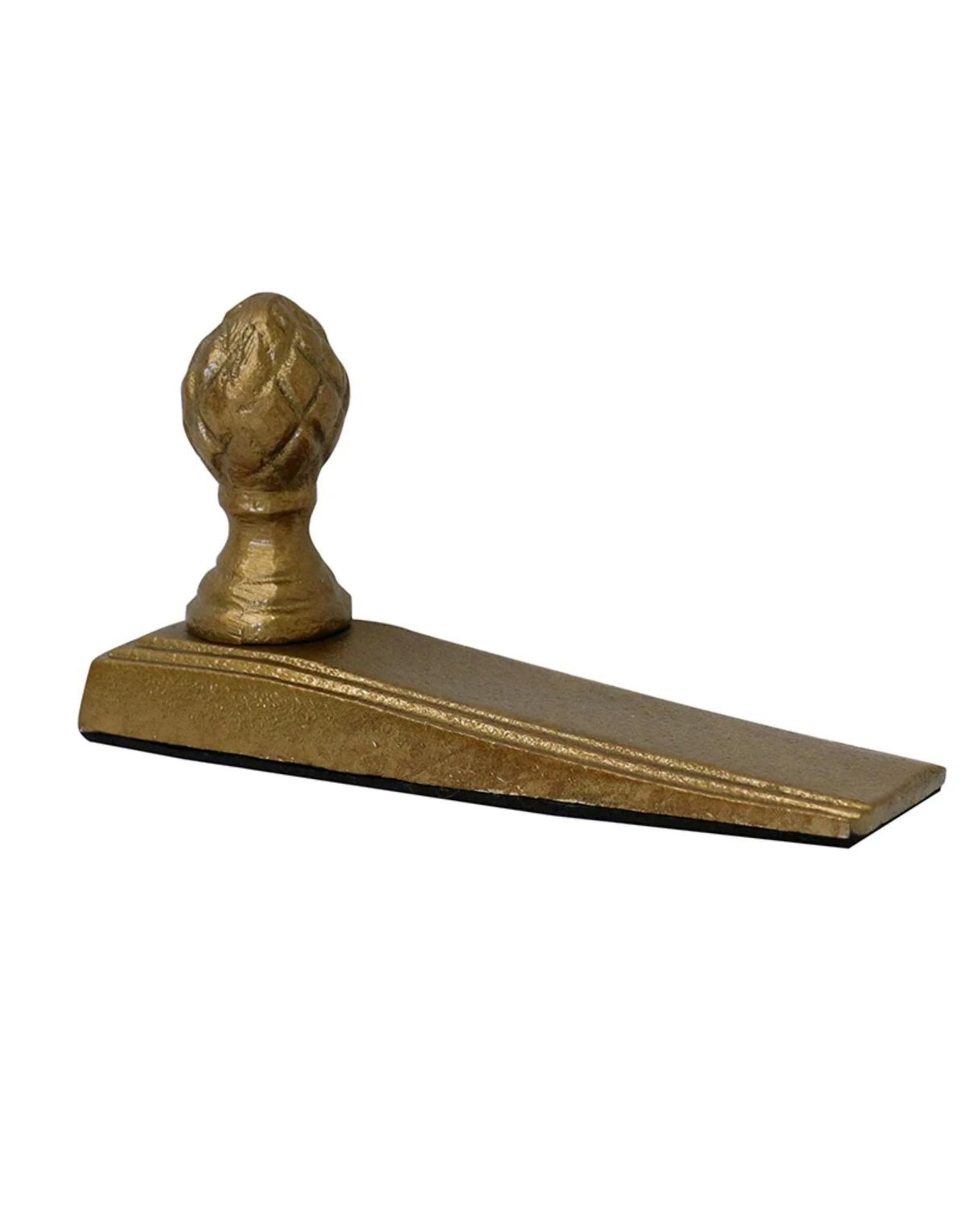 The ACORN DOOR STOP by CC interiors is a wedge-shaped doorstop with a brass finish, featuring an ornate decorative knob on top that combines an elegant design with durable construction.