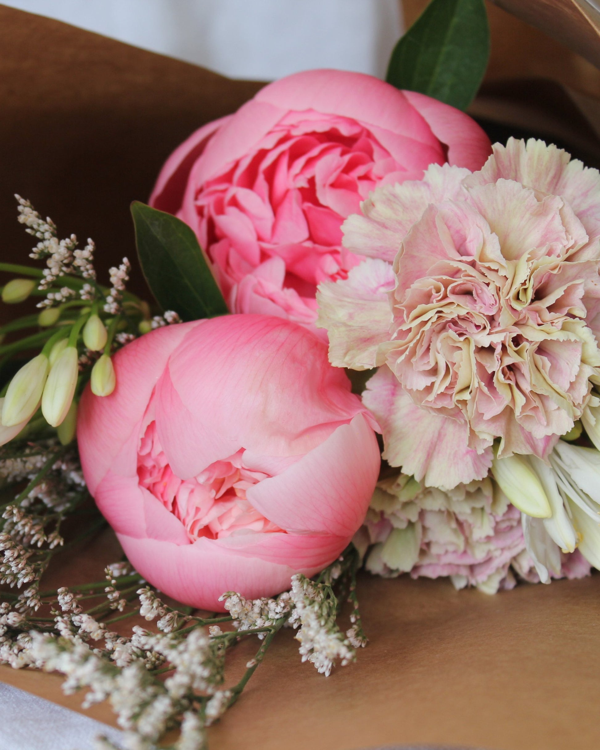 The Workroom NZ introduces the AMORE BASKET - FOR HER, showcasing a delightful arrangement of vibrant pink peonies, a soft pink carnation, and white buds, all elegantly wrapped in brown paper—perfect for enhancing a Bianca Lorenne gift basket.