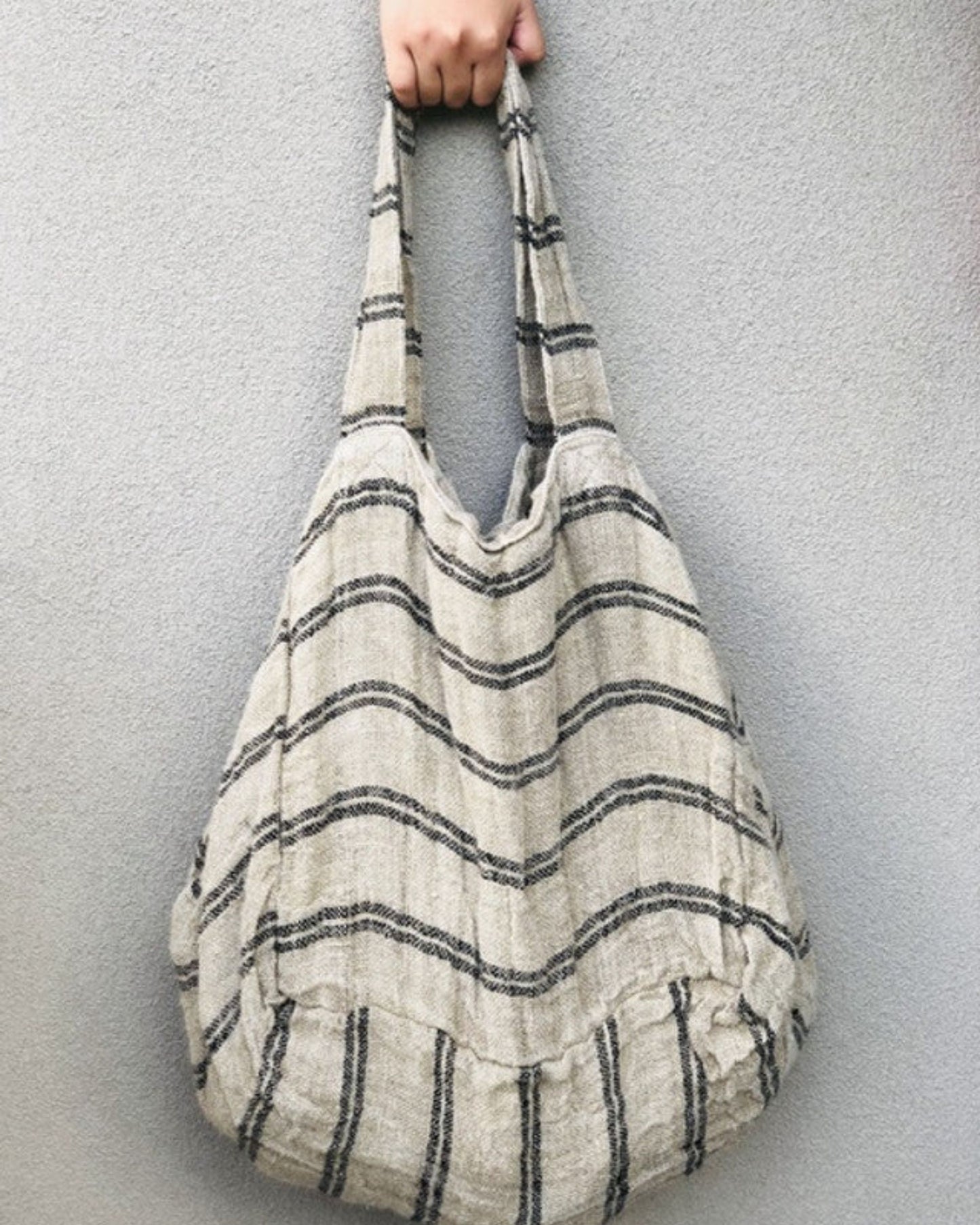 Against a gray background, a hand displays the ANGASTON BLACK STRIPE LINE TOTE BAG by Rustic Linen, highlighting its durable design with black and white striped patterns.