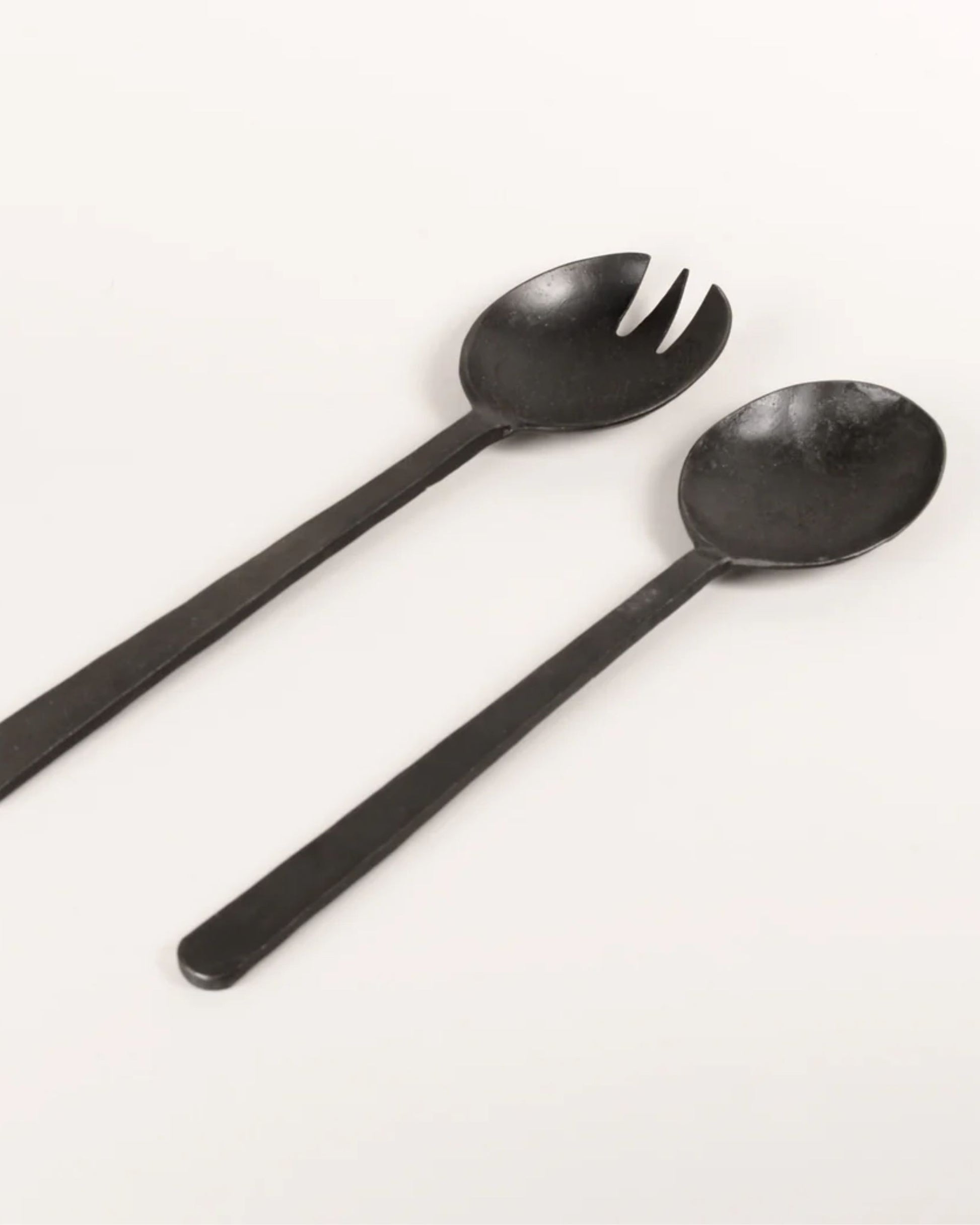 A photo of two *New direction* ANTIQUE FLAT HANDLE SERVING SPOONS featuring a fork with wide prongs and a spoon, both with long handles, placed parallel on a light surface.