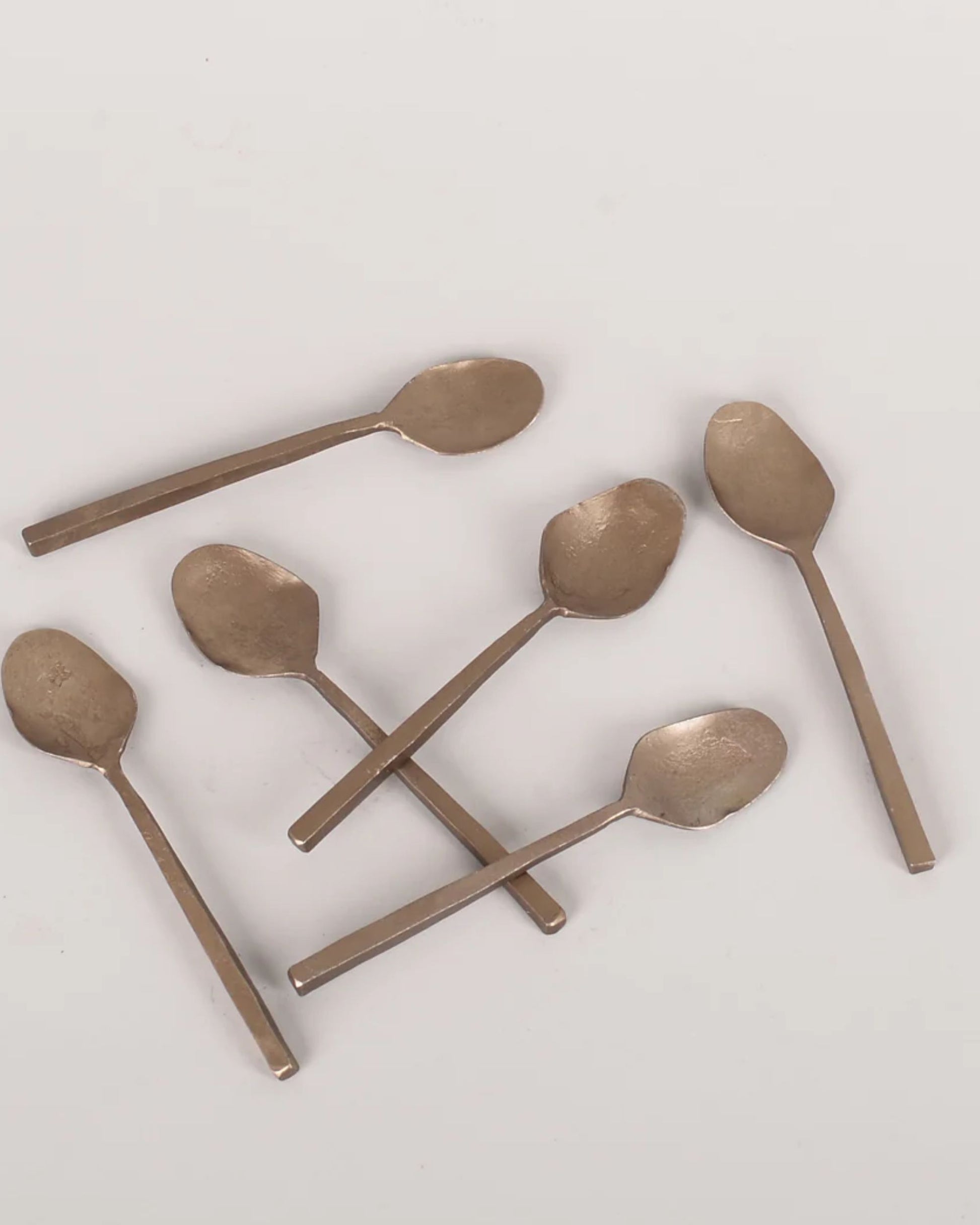 Six ANTIQUE SALT SPOONS from New direction, each exuding vintage charm, are arranged haphazardly on a plain white background.