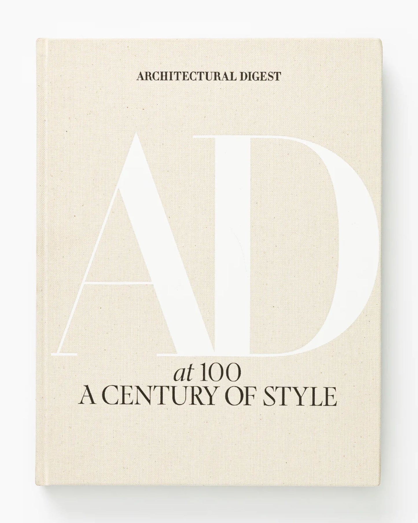 The book cover for "Architectural Digest at 100" by Bookreps features a beige background with "Architectural Digest" at the top. A large, white "AD" stands prominently in the center. Below, in smaller black text, it reads "At 100" and "A Century of Style," celebrating high-profile designers and timeless design styles.