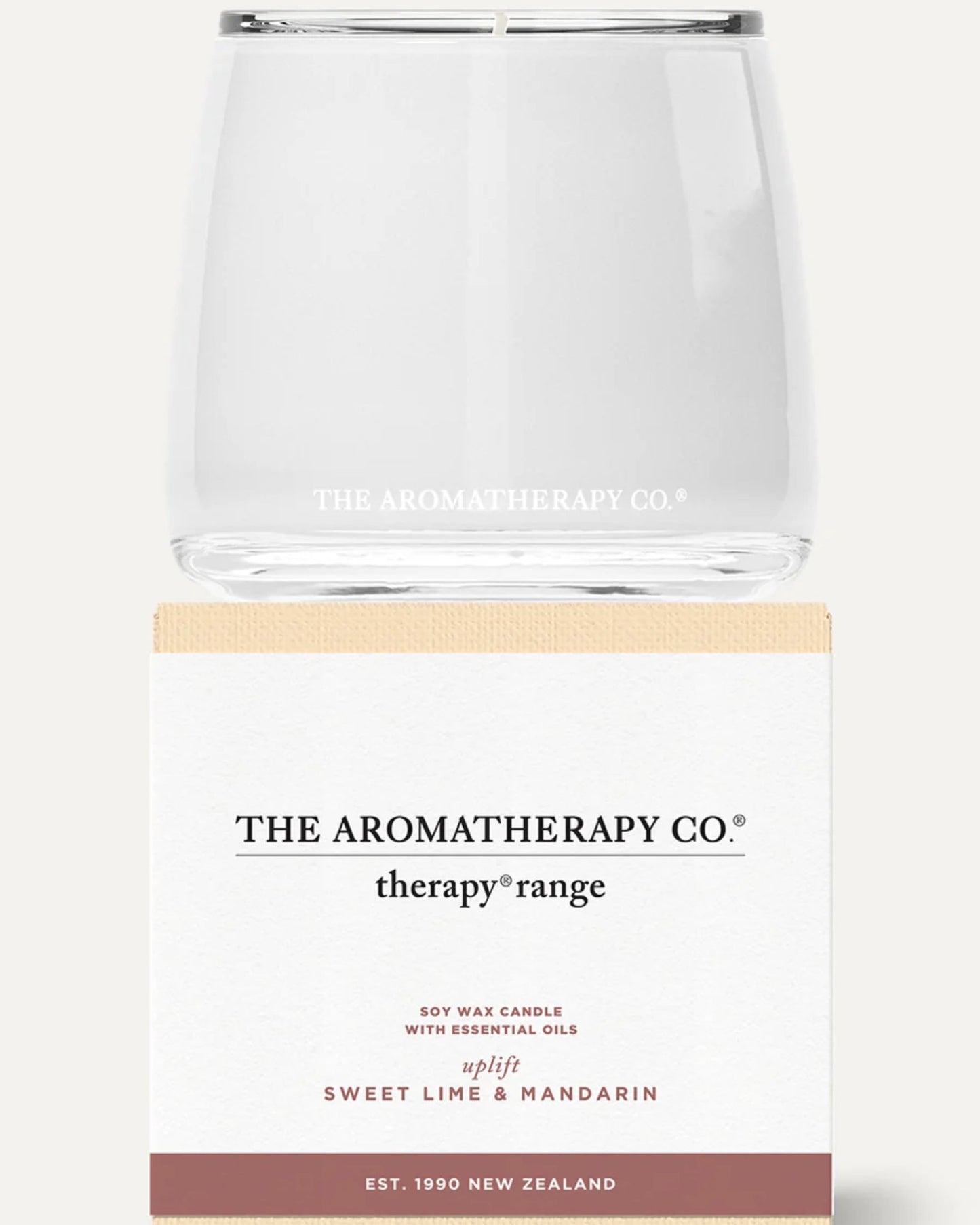 A clear jar candle from The Aromatherapy Co’s Therapy Range rests on its box. Crafted with soy wax and essential oils, it offers a Sweet Lime & Mandarin fragrance. Its minimalist design, showcased in light cream and brown tones, appeals to those who value high-quality aromatherapy candles.