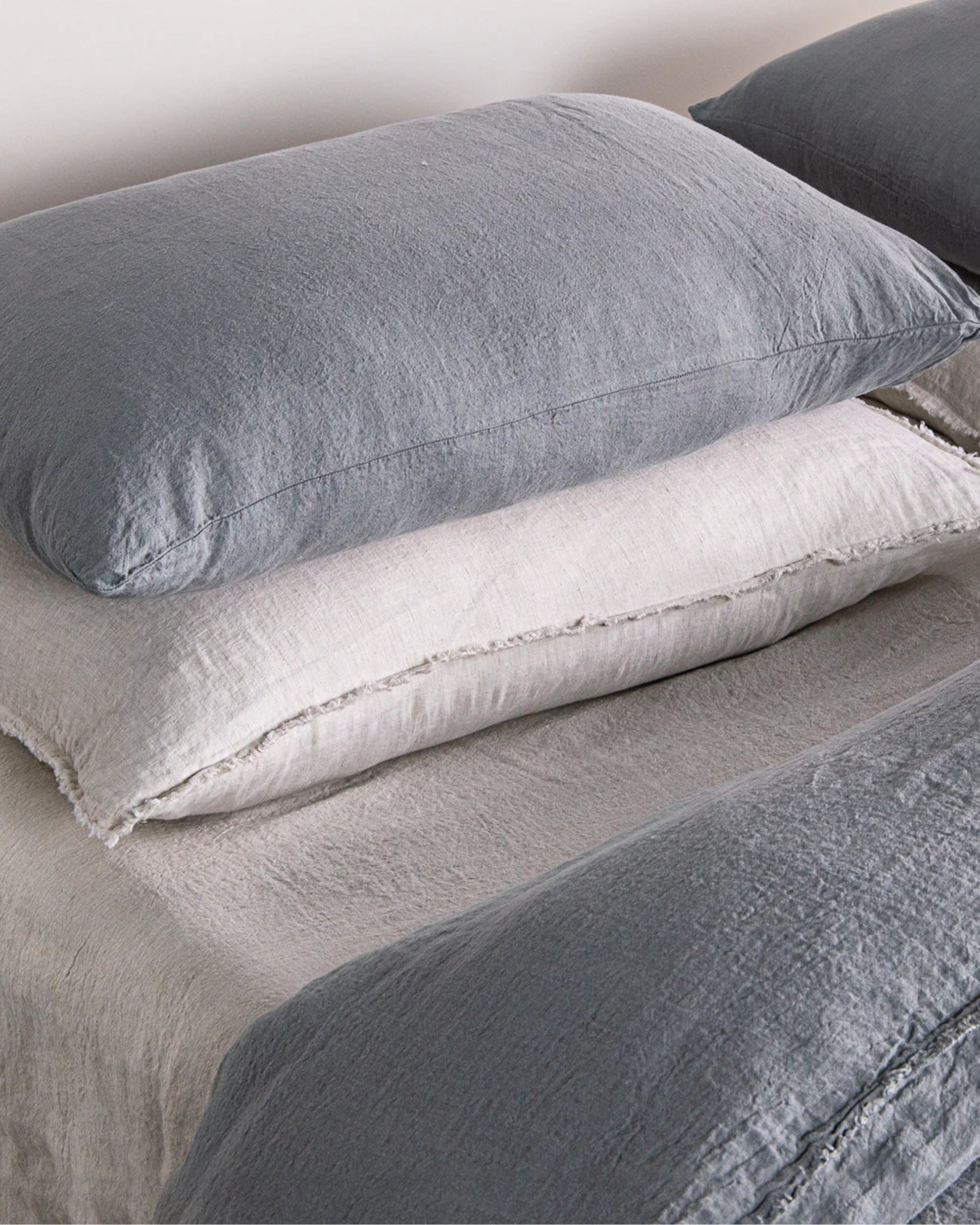 A neatly arranged set of pillows on a bed, featuring soft and textured gray and white BASIX STANDARD PILLOW CASE designs by Hale Mercantile Co.