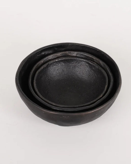 A set of three BLACK IRON BOWLs from New direction, exuding rustic charm, are elegantly stacked on a plain white background. These circular beauties feature a smooth yet subtly textured surface, reminiscent of a handmade piece crafted with care and precision.